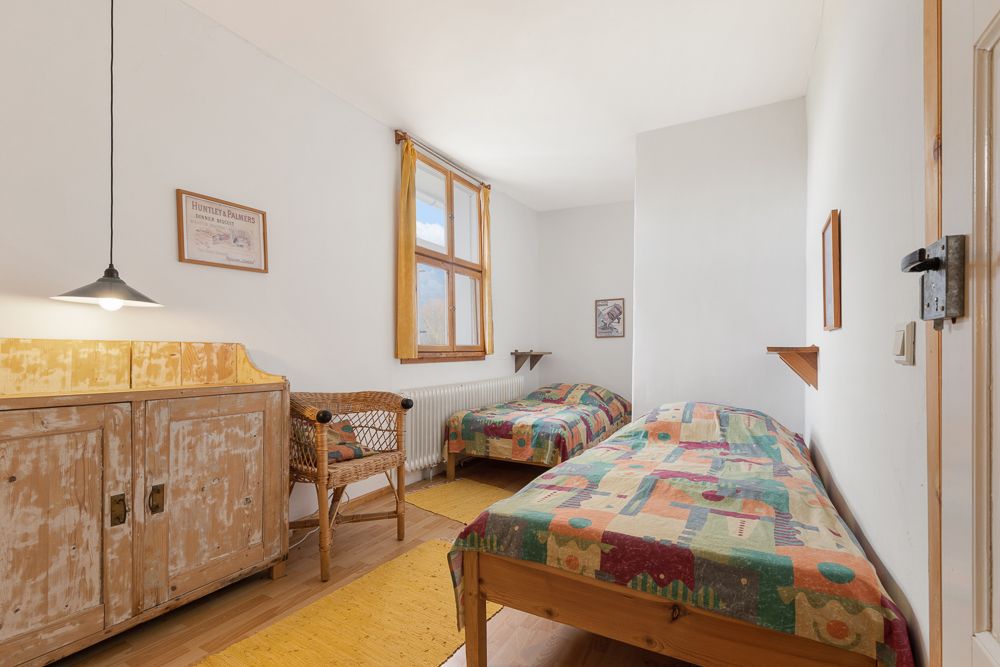 Schlafzimmer mit zwei Einzelbetten, bunten Bettdecken, Fenster und rustikalem Holzschrank.