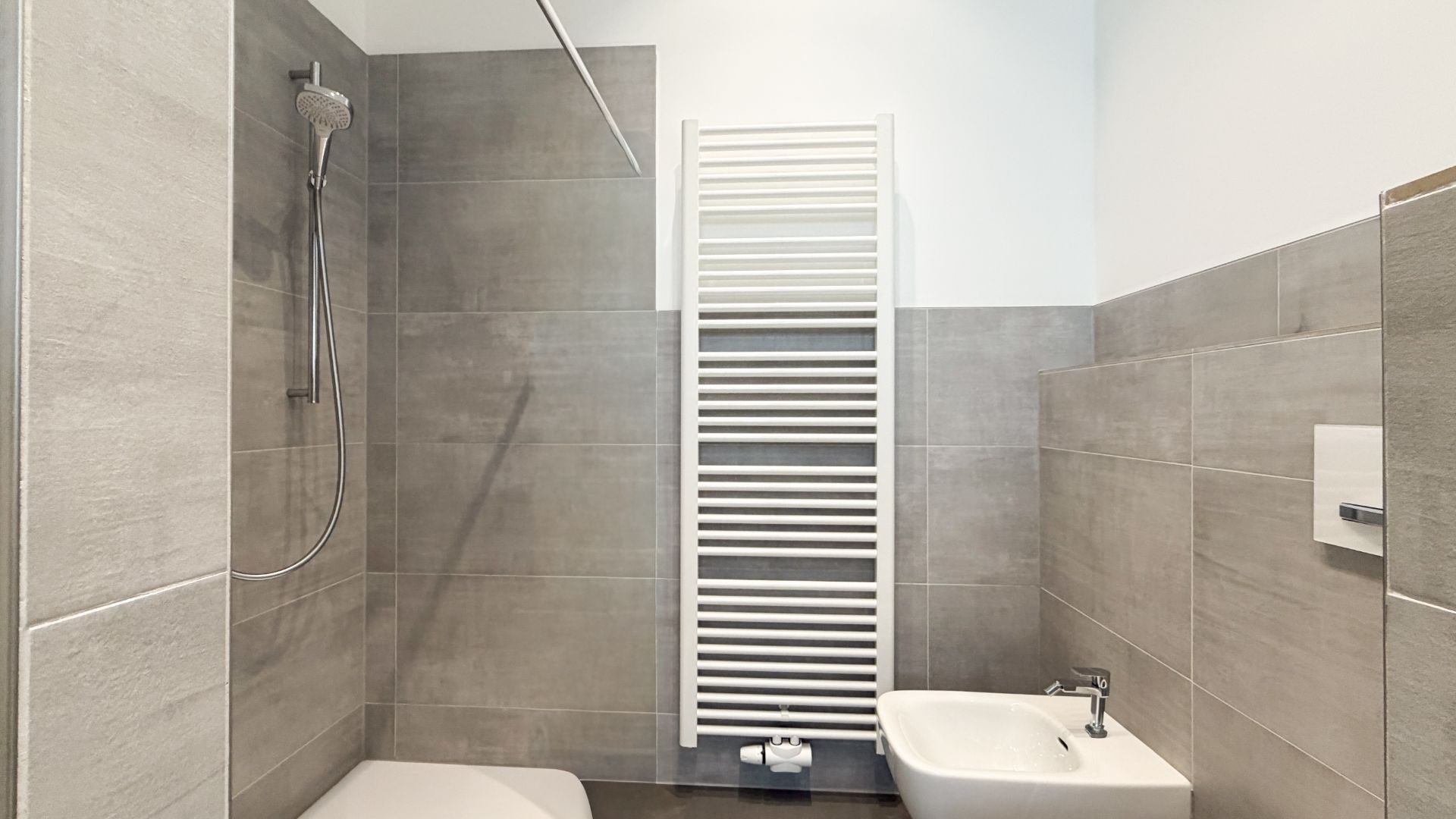 Modernes Badezimmer mit Dusche, Bidet, weißen Fliesen und Handtuchheizkörper.