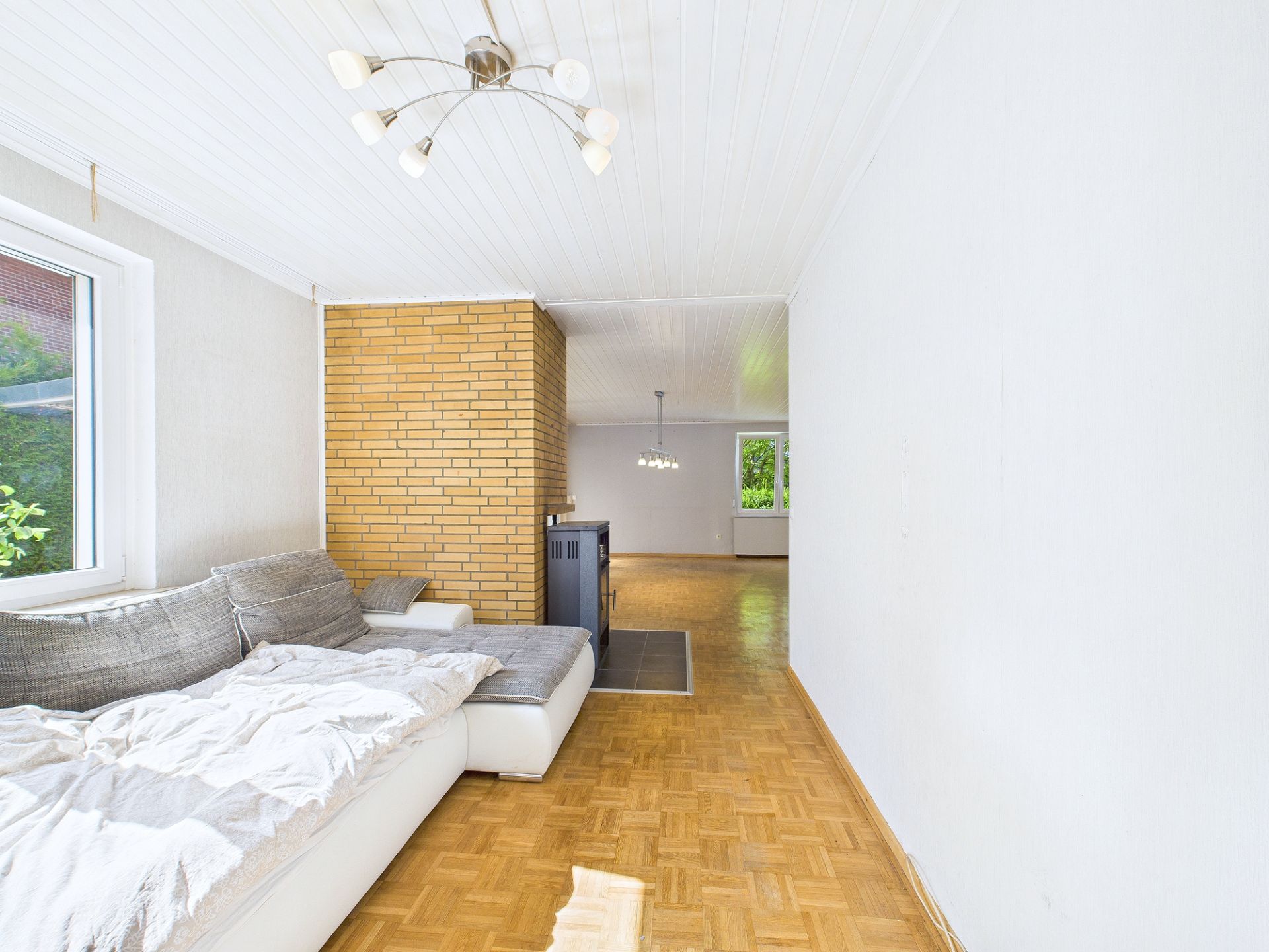 Helles Wohnzimmer mit Ecksofa, Parkettboden und Backsteinwand.