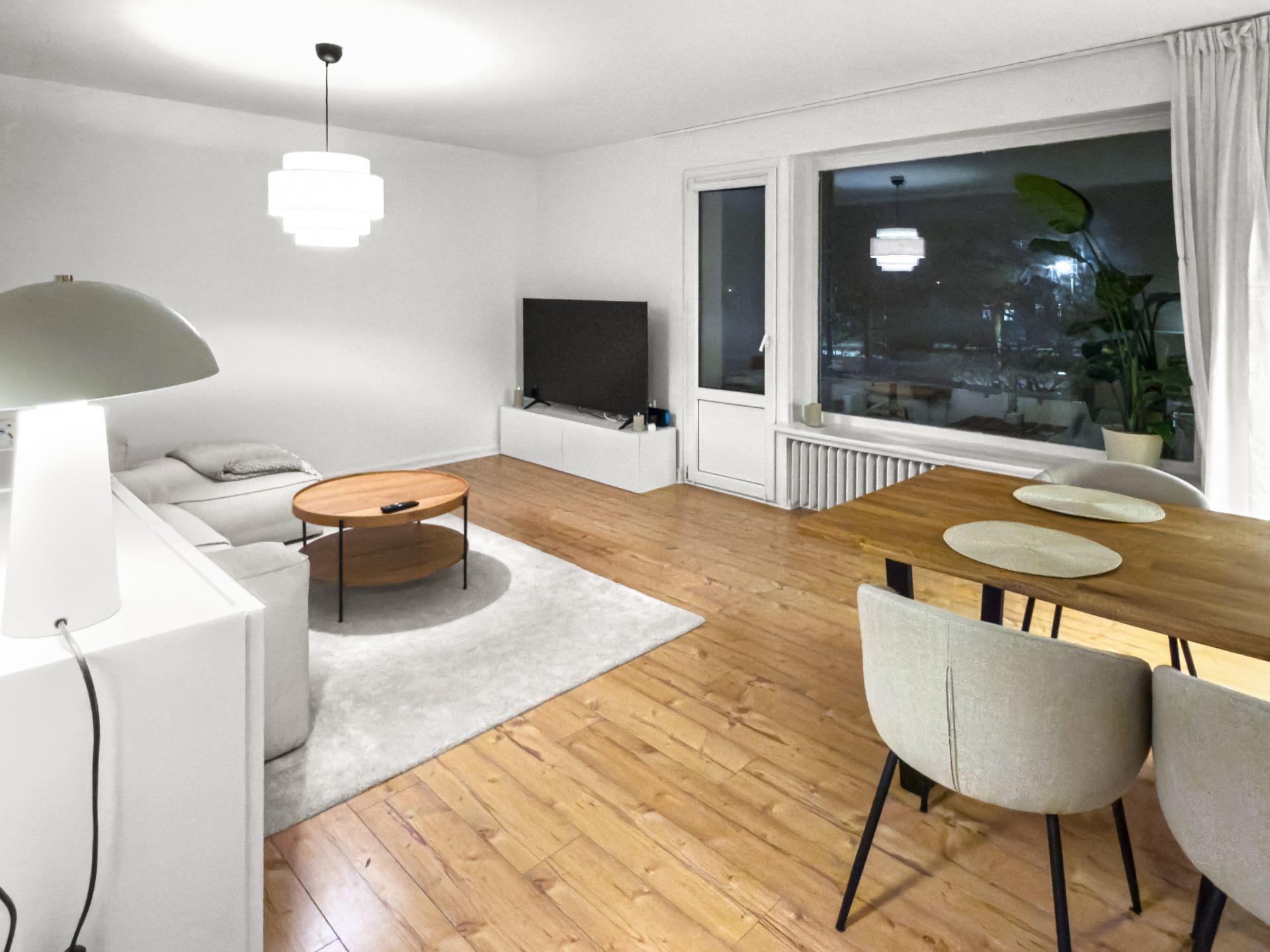 Modernes Wohnzimmer mit Ecksofa, Fernseher, Esstisch und großem Fenster.