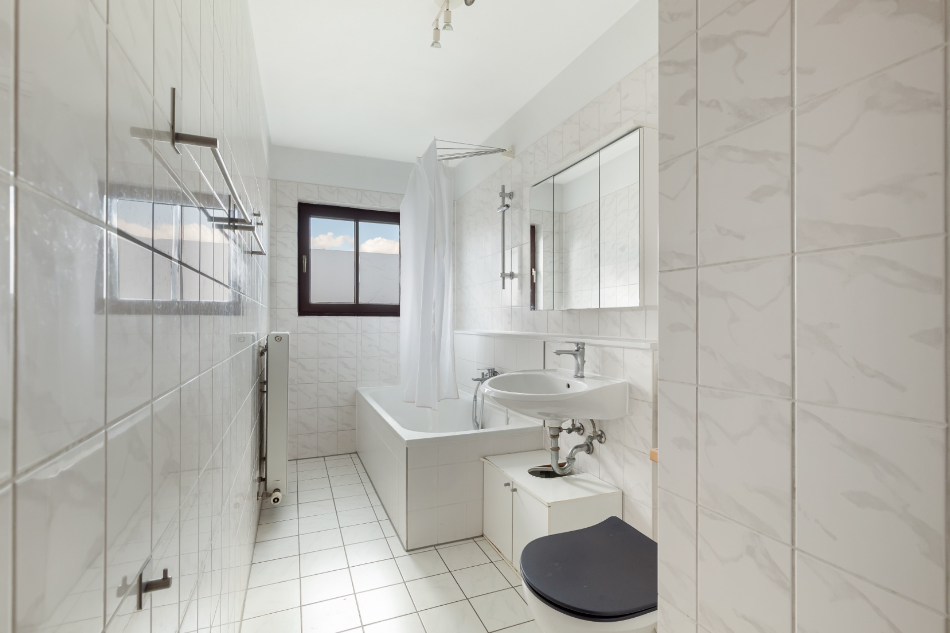 Helles Badezimmer mit Badewanne, weißem Fliesenspiegel, Fenster und Waschbecken.