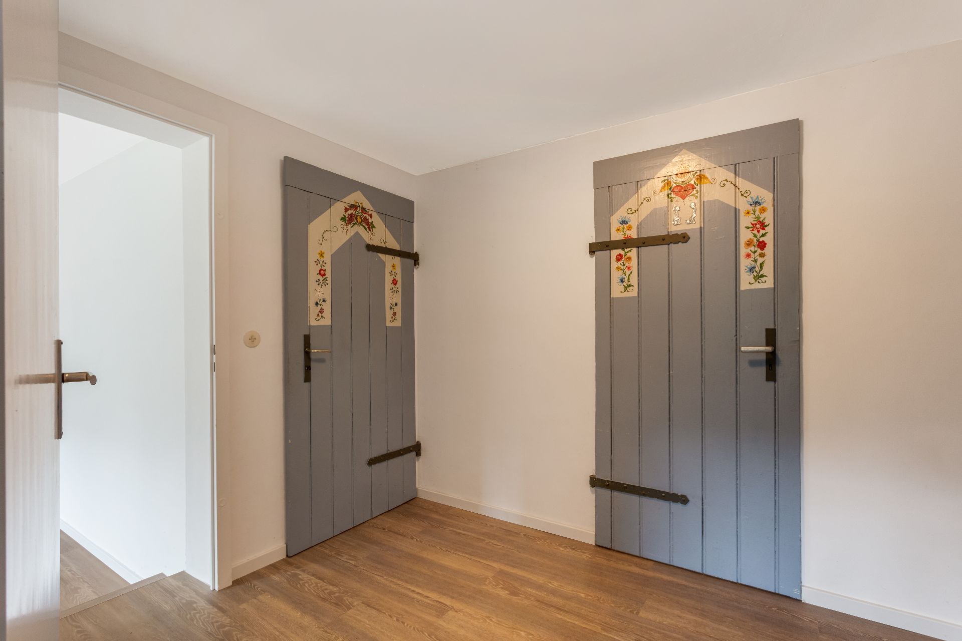Raum mit zwei grauen Holztüren, verziert mit bunten Blumenmustern, und hellem Holzboden.