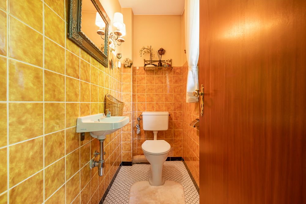 Kleines Badezimmer mit gelben Fliesen, WC, Waschbecken, Spiegel und Fenster.