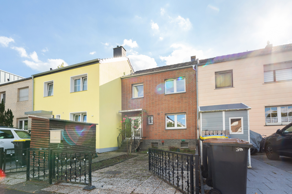 Reihenhaus mit roter Backsteinfassade, Vorgarten und Mülltonnen vor dem Haus.