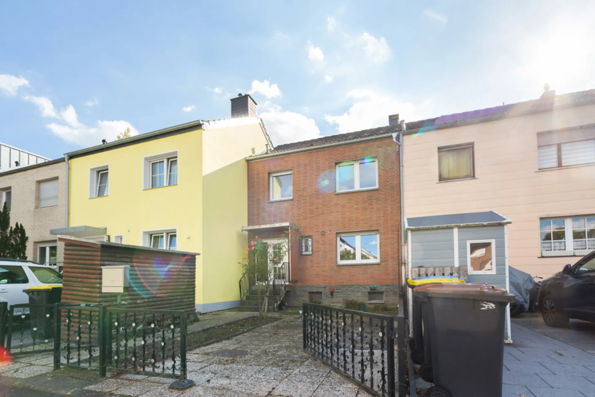 Reihenhaus mit roter Backsteinfassade, Vorgarten und Mülltonnen vor dem Haus.