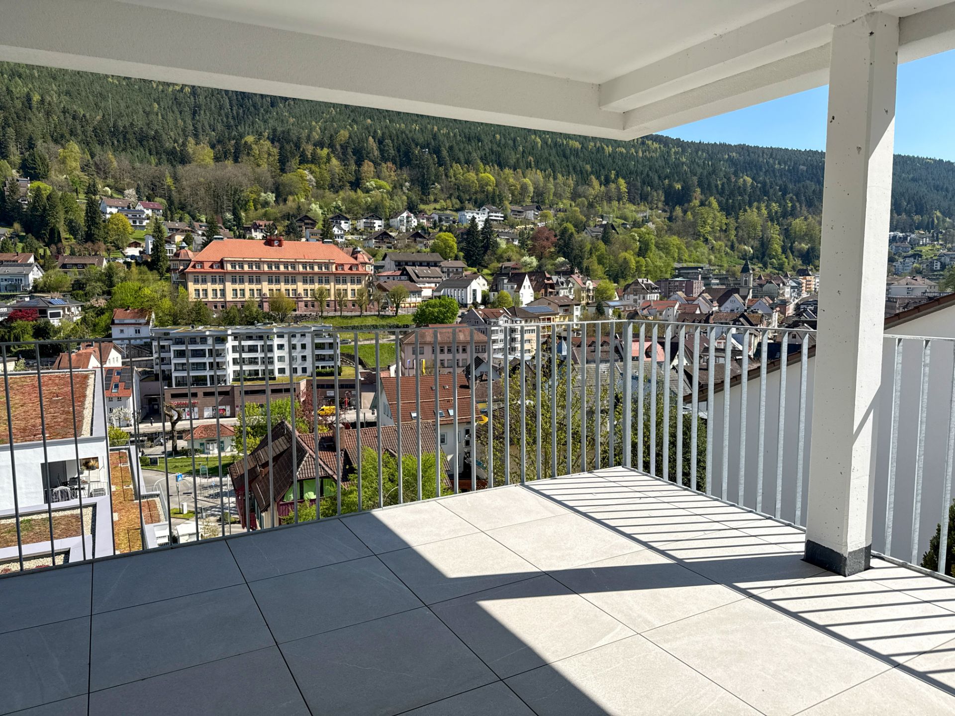 Überdachter Balkon mit Fliesenboden und Blick auf eine Stadt und bewaldete Hügel.
