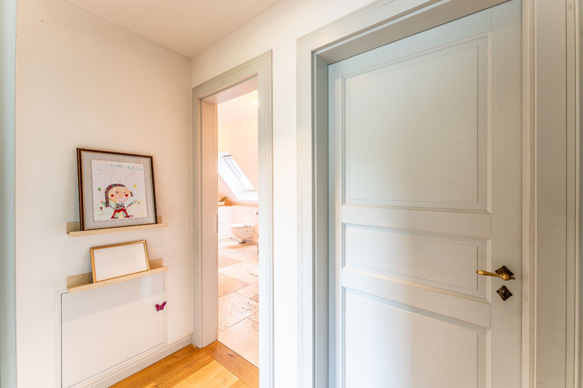 Flur mit weißen Türen, Kinderzeichnung an der Wand, Blick ins Badezimmer mit Fenster.
