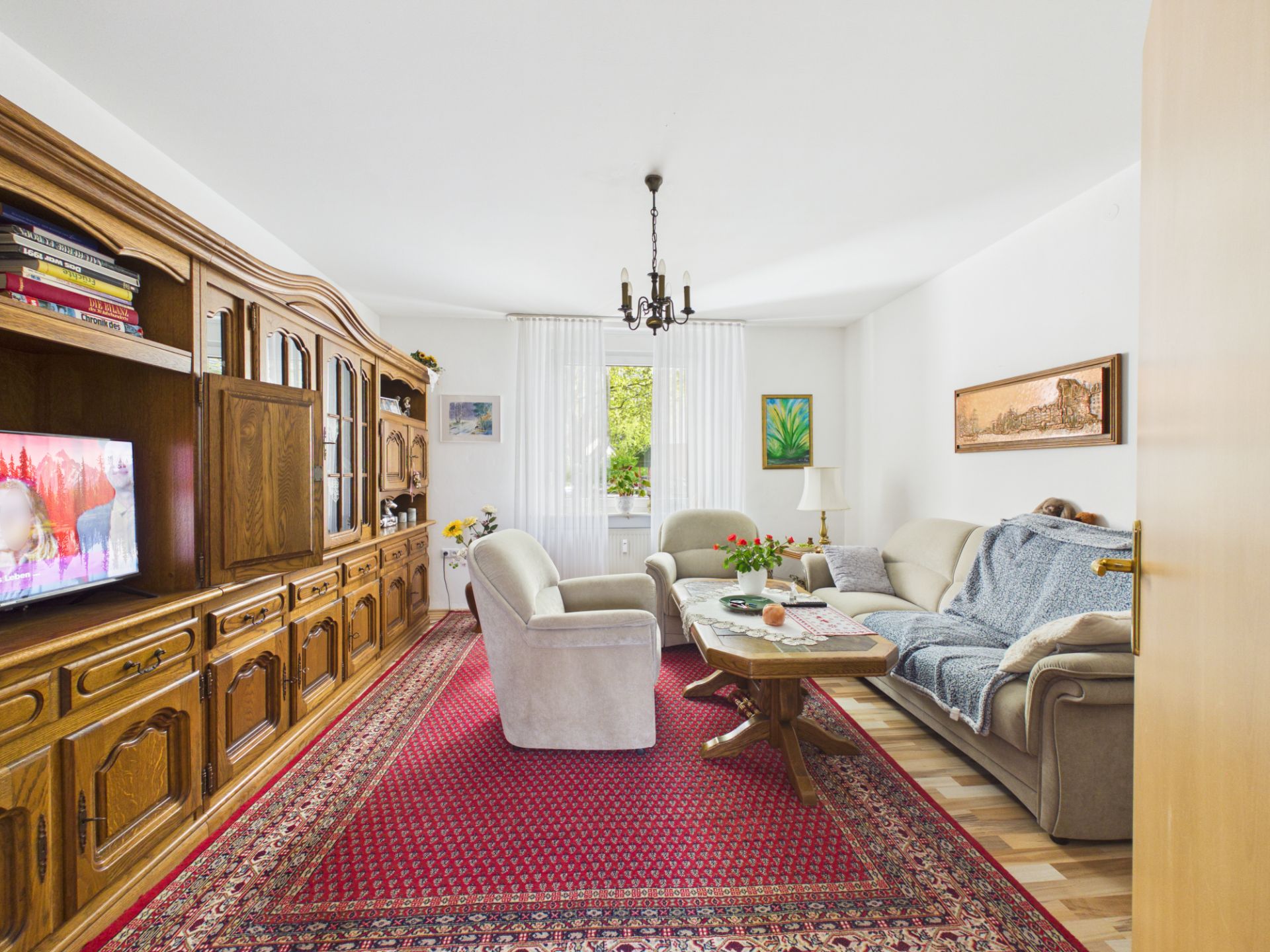 Wohnzimmer mit Holzschrankwand, Sofas, Couchtisch und rotem Teppich.