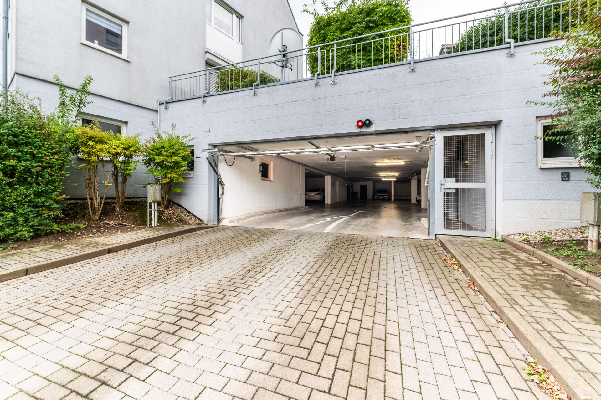 Einfahrt zu einer Tiefgarage mit offenen Toren und gepflastertem Hof.