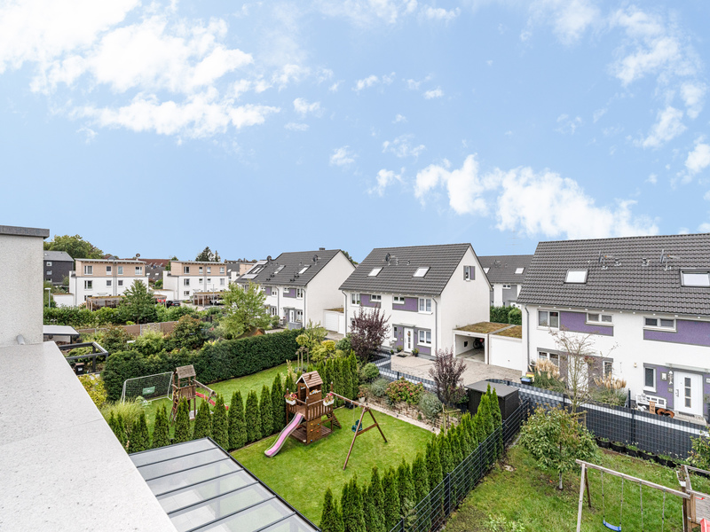 Reihenhäuser mit Gärten und Spielplatz im Hintergrund, blauer Himmel mit wenigen Wolken.