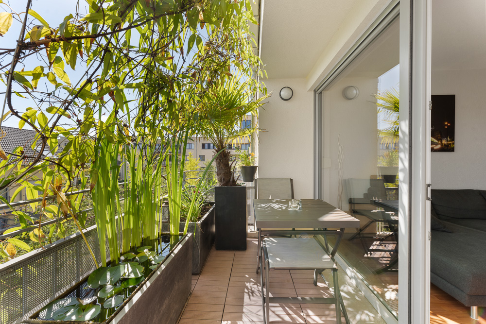 Balkon mit Holzboden, Tisch, Stühlen und vielen grünen Pflanzen, Zugang vom Wohnzimmer.