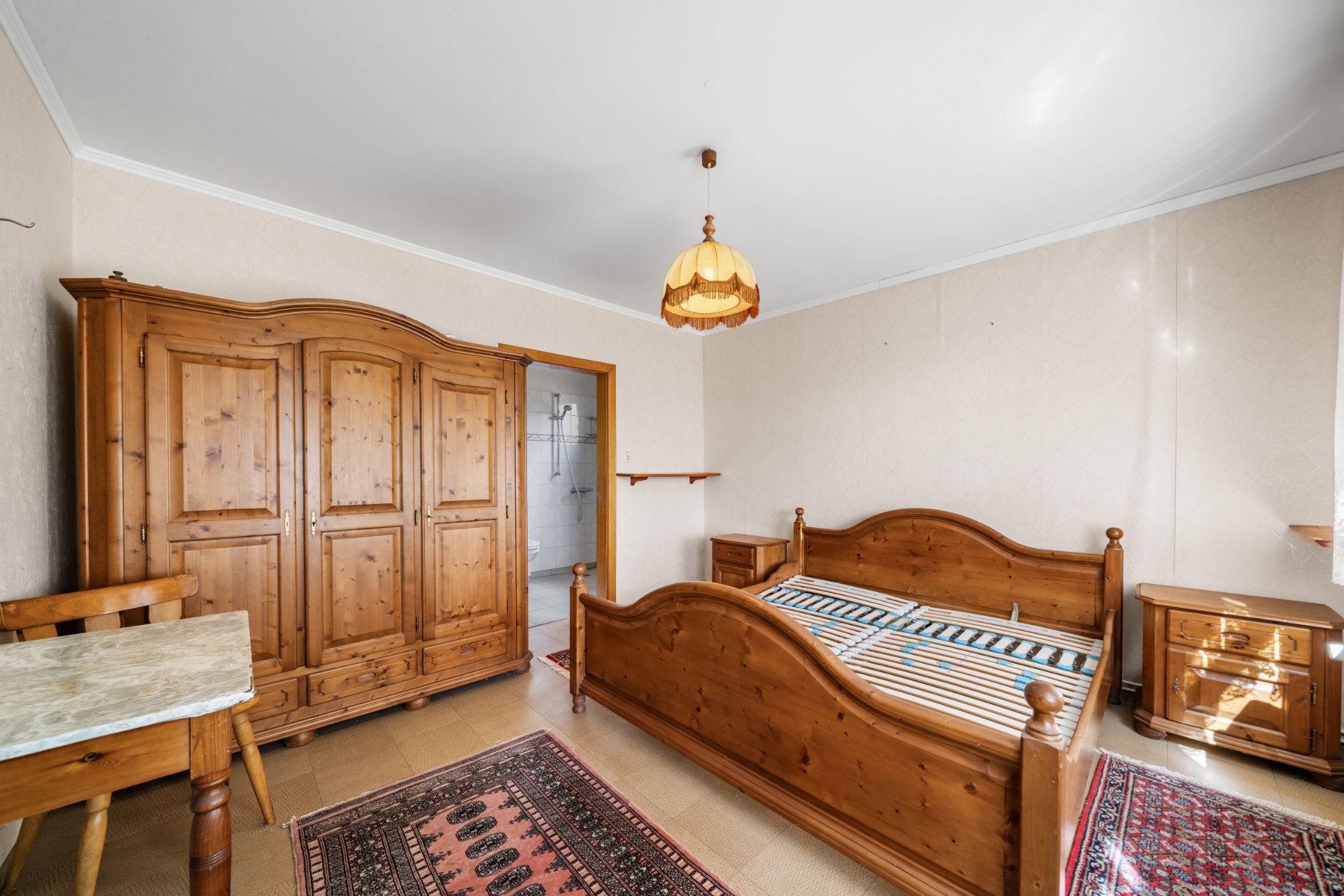 Schlafzimmer mit Holzbett, Kleiderschrank, Nachttischen, Schreibtisch und Teppichen.