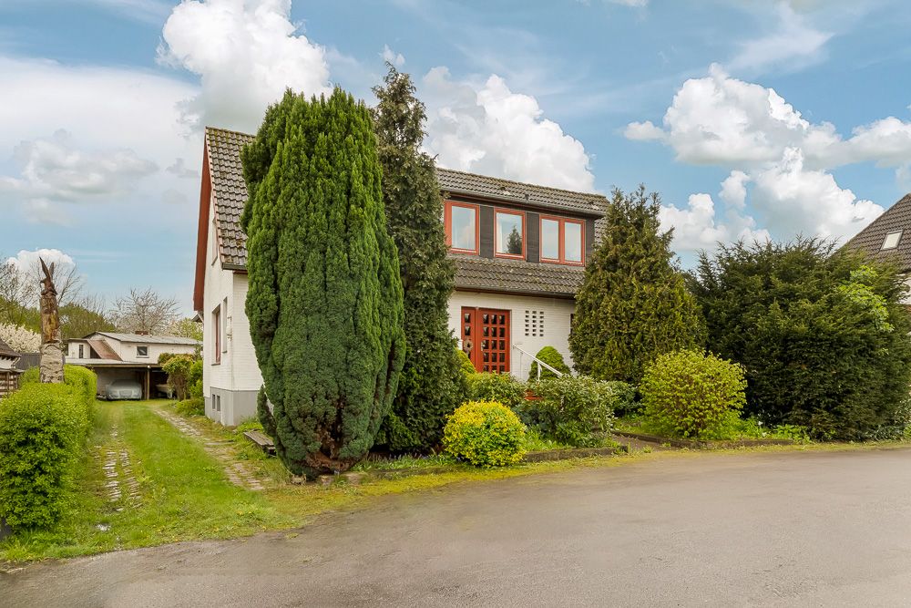 Zweistöckiges Wohnhaus mit Satteldach und großem Garten, umgeben von vielen Büschen und Bäumen.