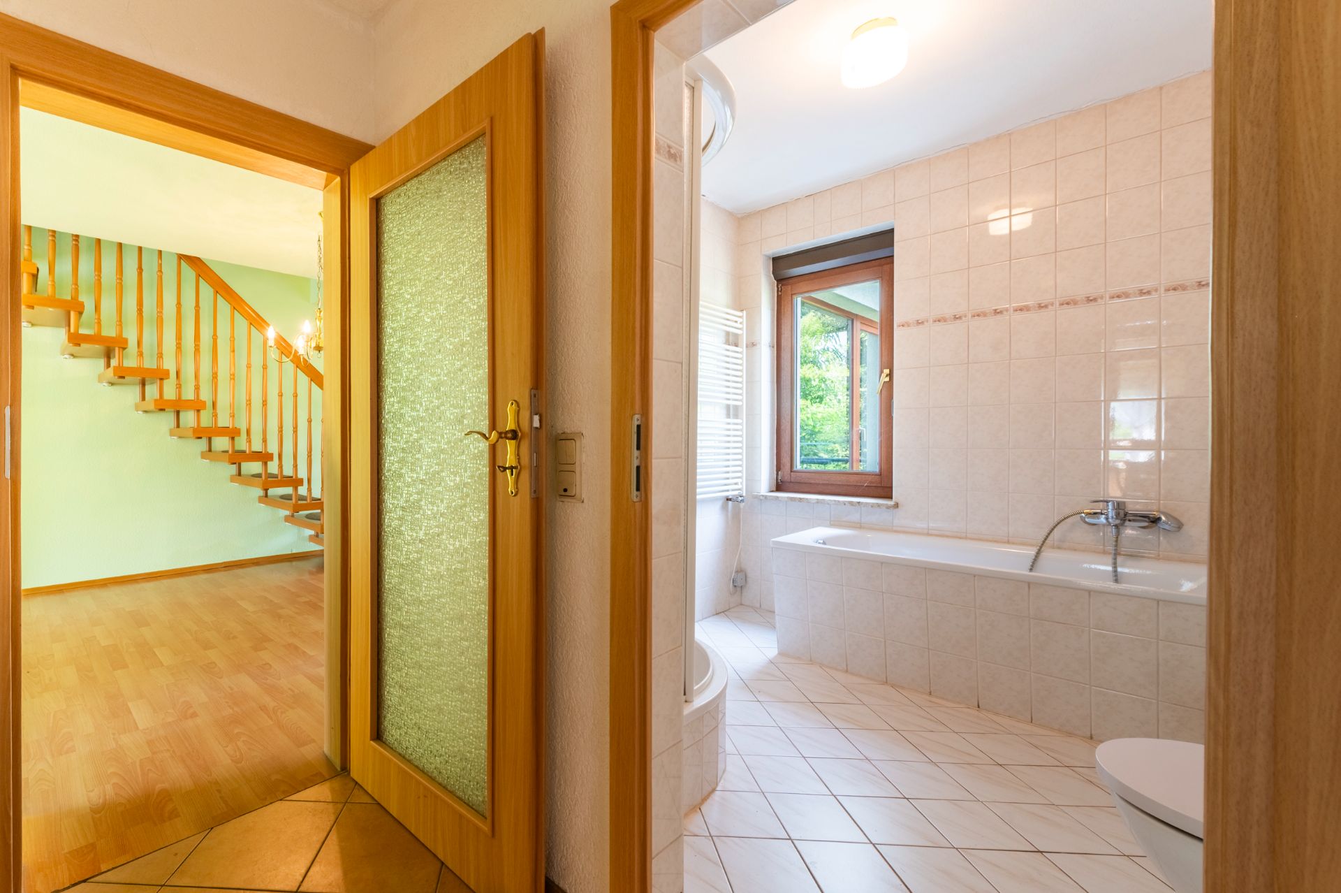 Flur mit Blick ins Badezimmer mit Badewanne und in ein Wohnzimmer mit Holztreppe.