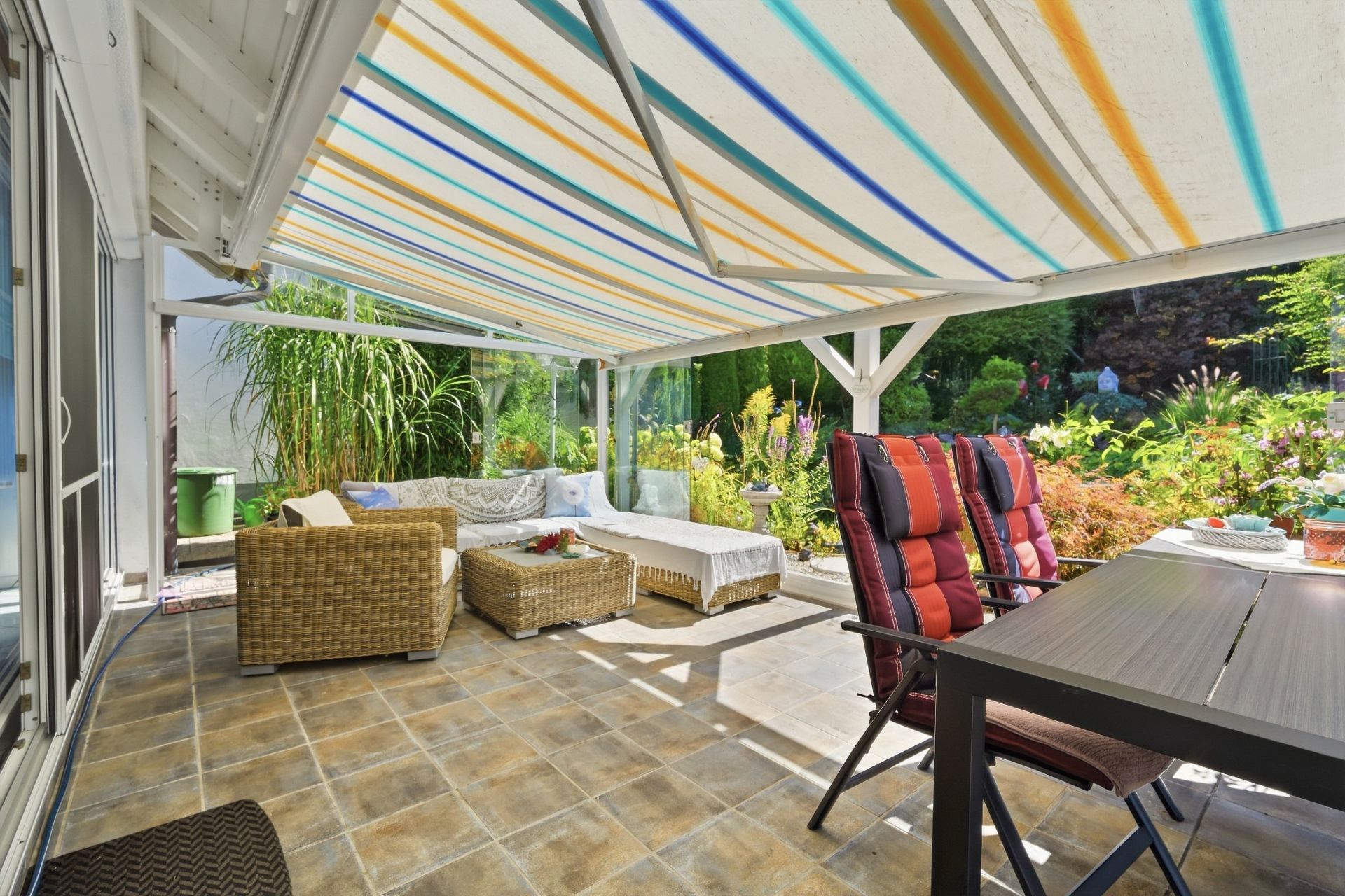Überdachte Terrasse mit Sitzgruppe, Esstisch und Blick auf einen Garten.