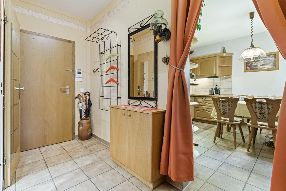 Flur mit Spiegel, Garderobe, Schirmständer und Blick in eine helle Küche mit Esstisch.