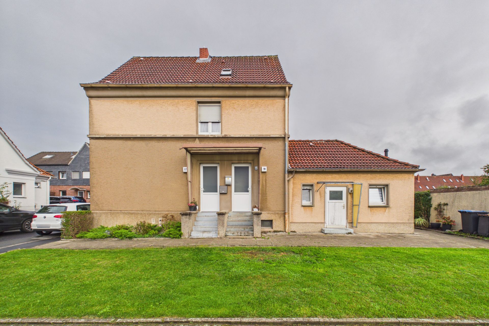 Zweistöckiges Wohnhaus mit rotem Dach, zwei Eingängen und gepflegtem Vorgarten.