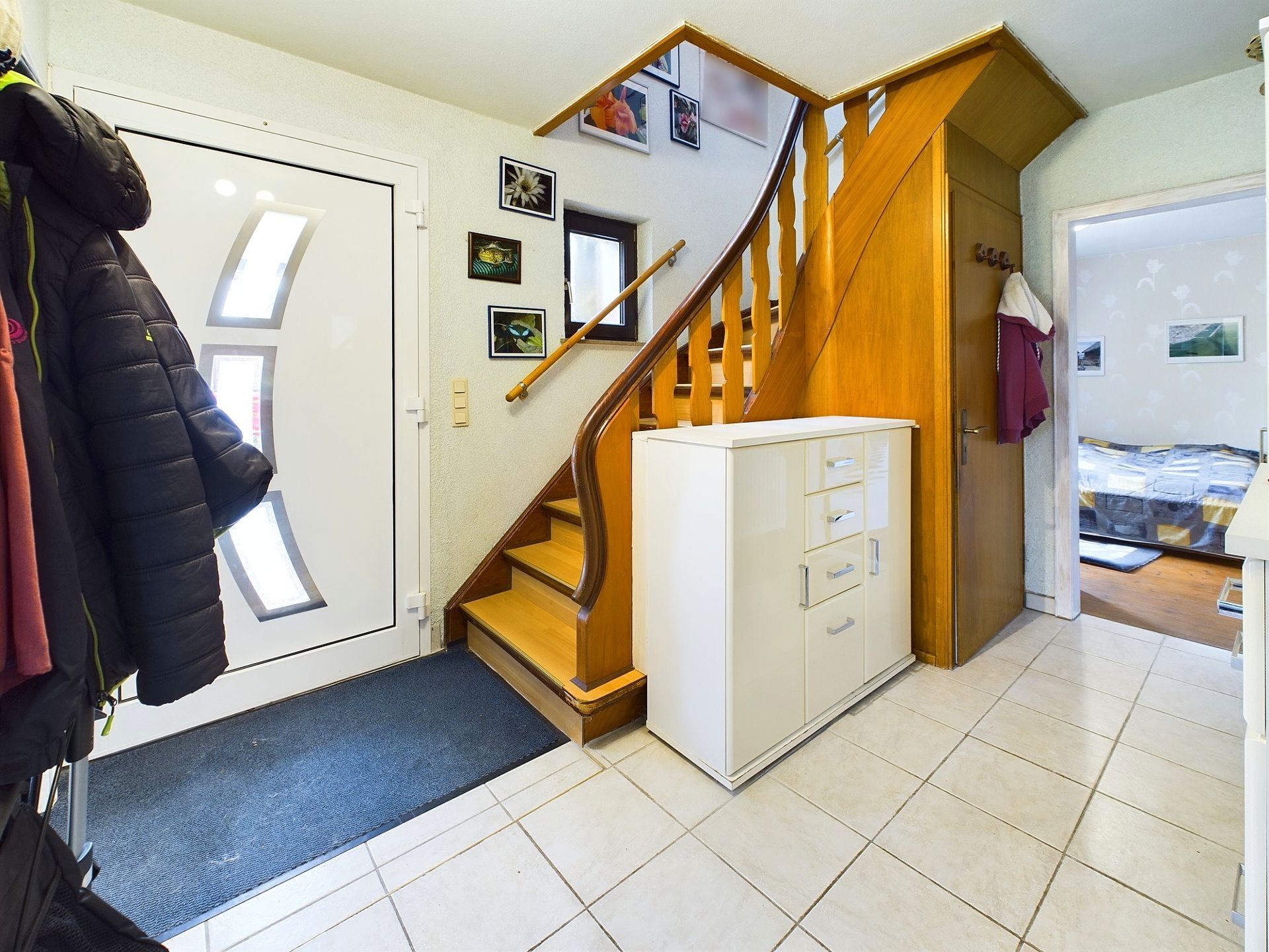 Flur mit Treppe aus Holz, weißem Schrank und Eingangstür mit Glas.