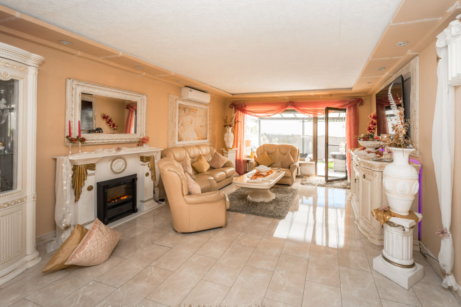 Helles Wohnzimmer mit beigen Ledersofas, Kamin, großen Fenstern und eleganter Dekoration.