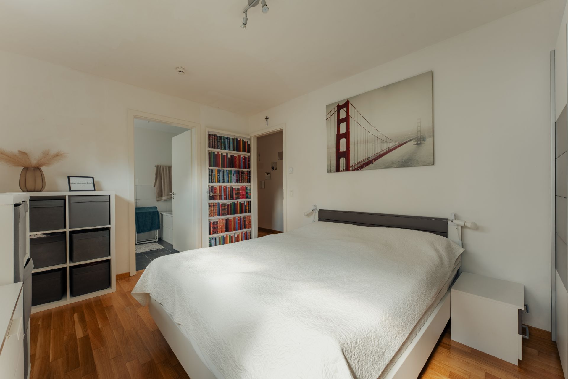 Helles Schlafzimmer mit Doppelbett, Nachttisch und Regal, Bild einer Brücke an der Wand.