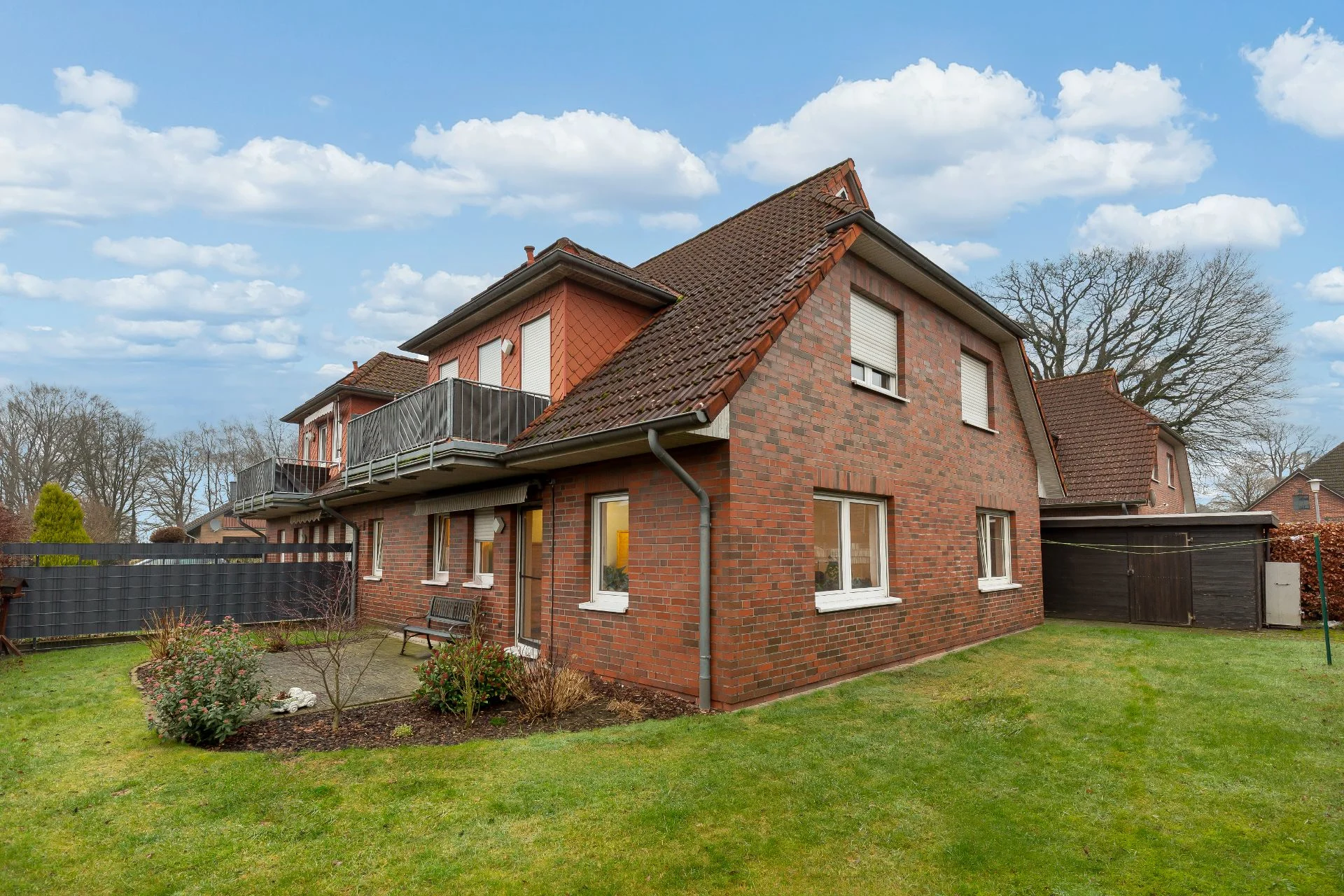 Backsteinhaus mit Satteldach, Balkon und Garten, neben weiteren Wohnhäusern.