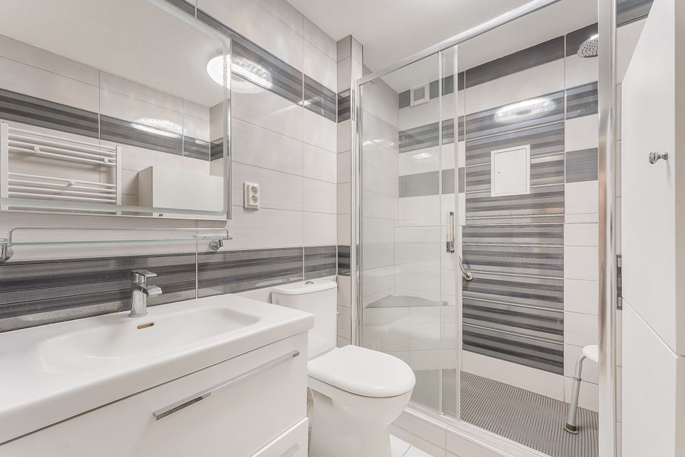 Modernes Badezimmer mit weißem Waschbecken, Toilette und großer Dusche mit Glastür.