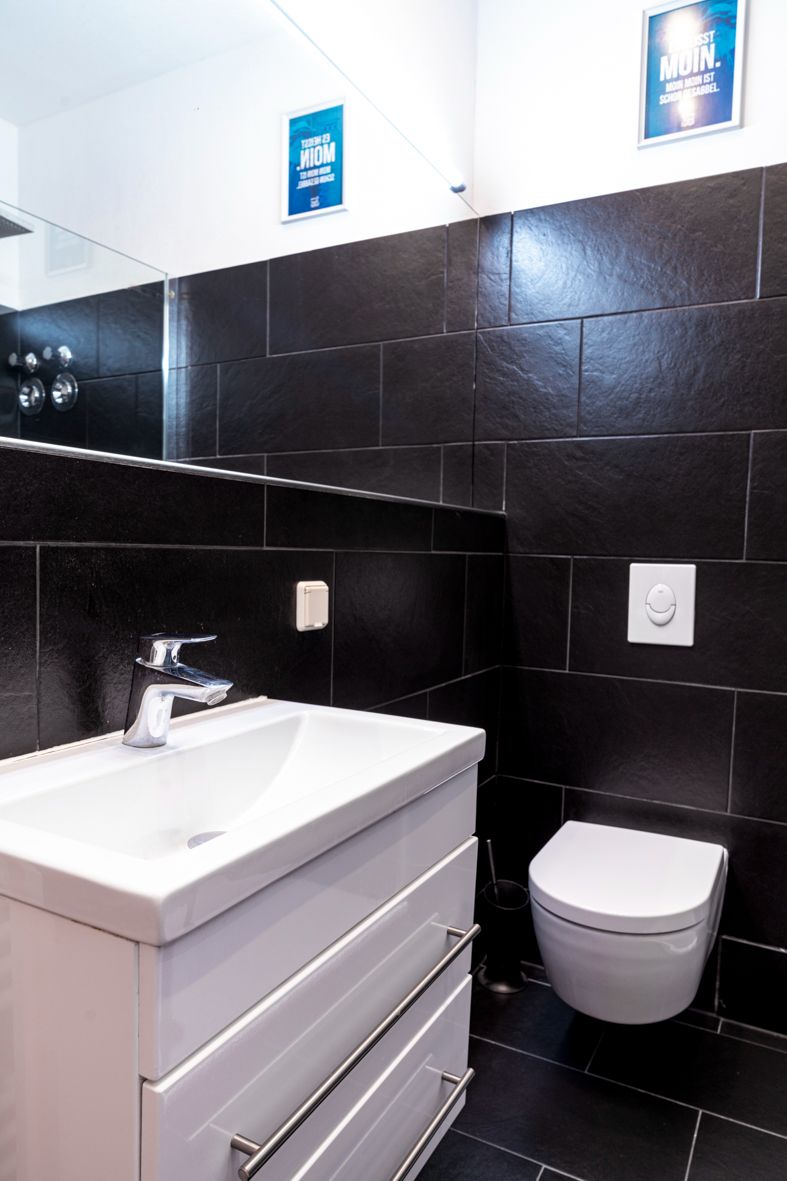 Modernes Badezimmer mit dunklen Fliesen, weißem Waschbecken und Wandtoilette.