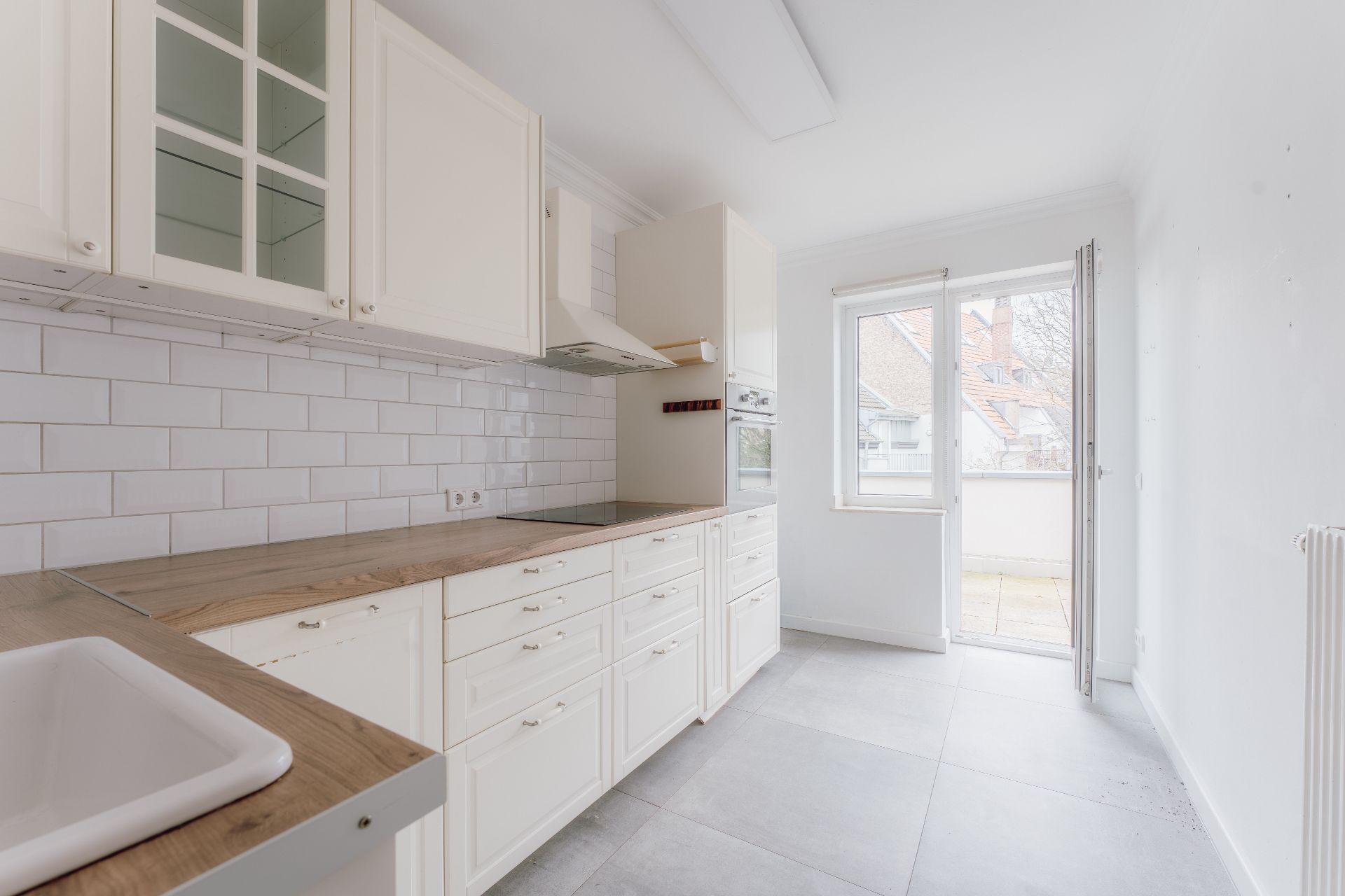 Helle Küche mit weißen Schränken, Holzarbeitsplatte und Zugang zum Balkon.