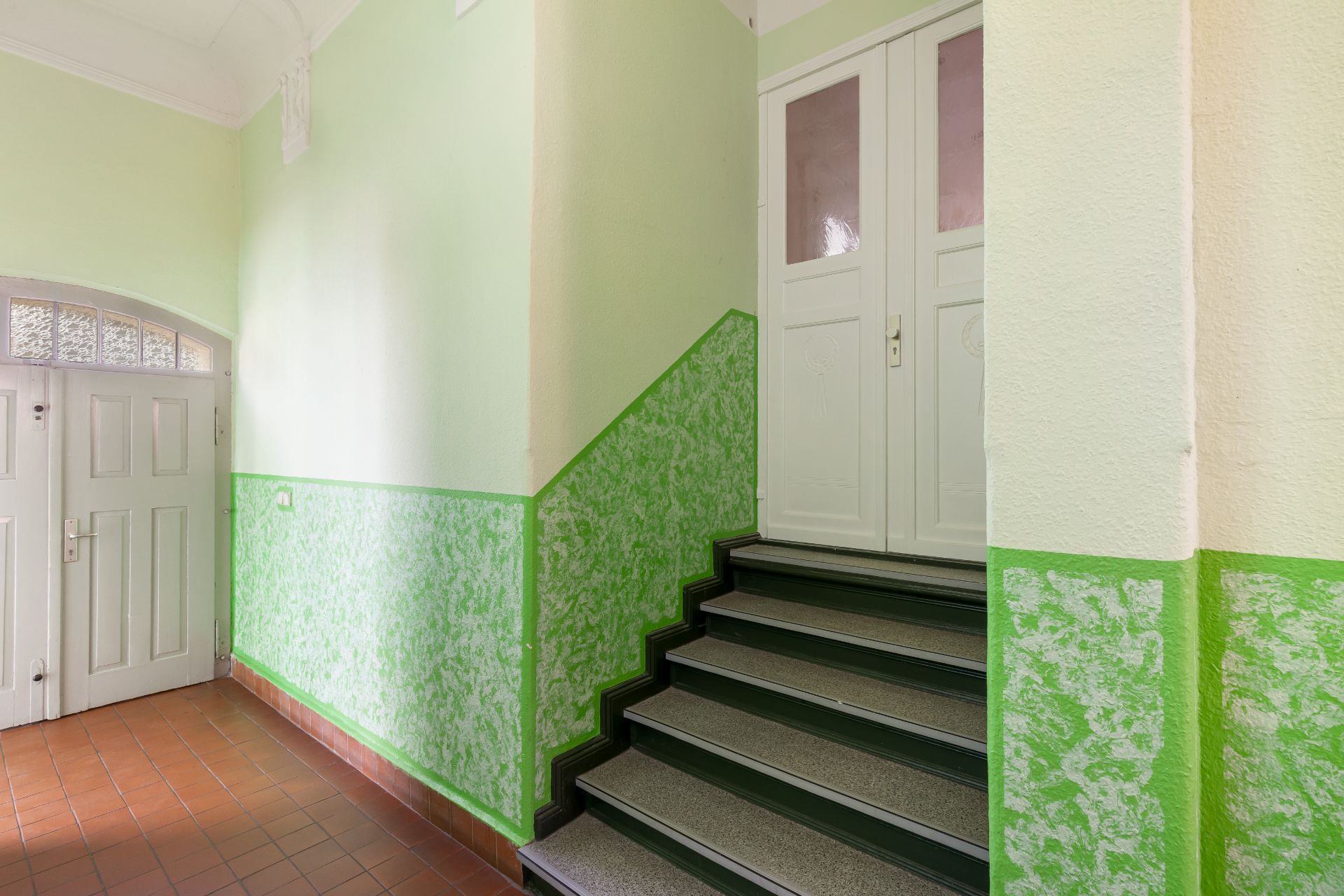 Heller Hausflur mit grüner Wand, Treppe und weißen Türen.