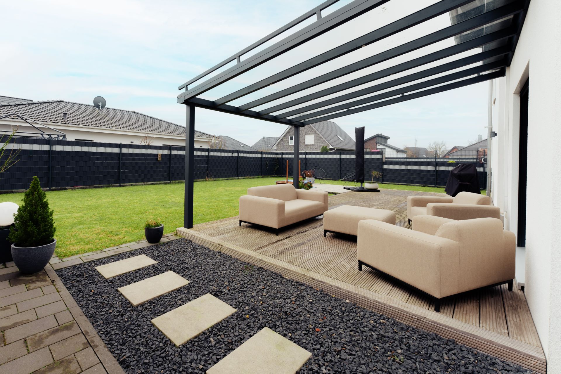 Überdachte Terrasse mit beigen Sitzmöbeln, Holzboden und Blick auf den Garten eines Wohnhauses.