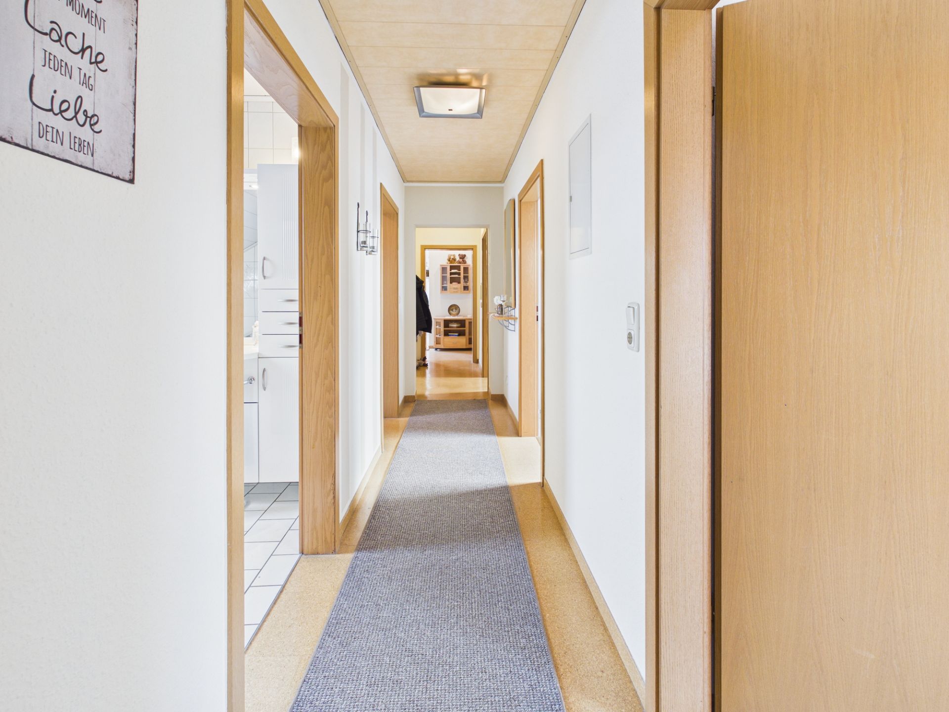 Langer, heller Flur mit Teppich und mehreren offenen Türen in einer Wohnung.