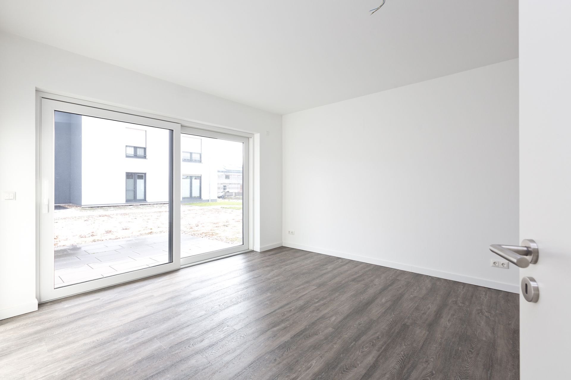 Leerer, heller Raum mit Holzboden und großer Glasschiebetür zum Garten.