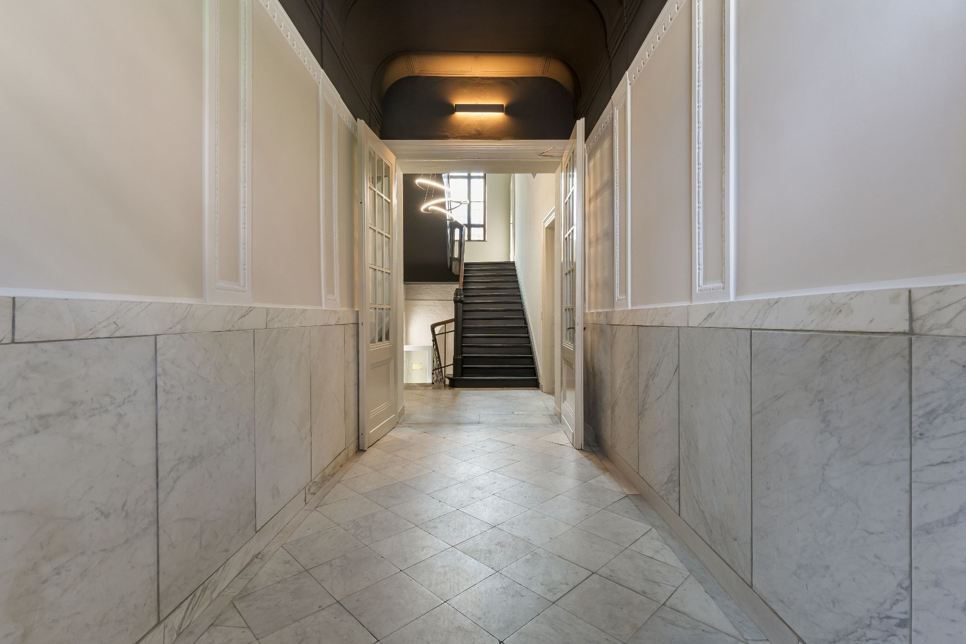 Heller Flur mit Marmorboden und offener Tür, dahinter eine Treppe nach oben.