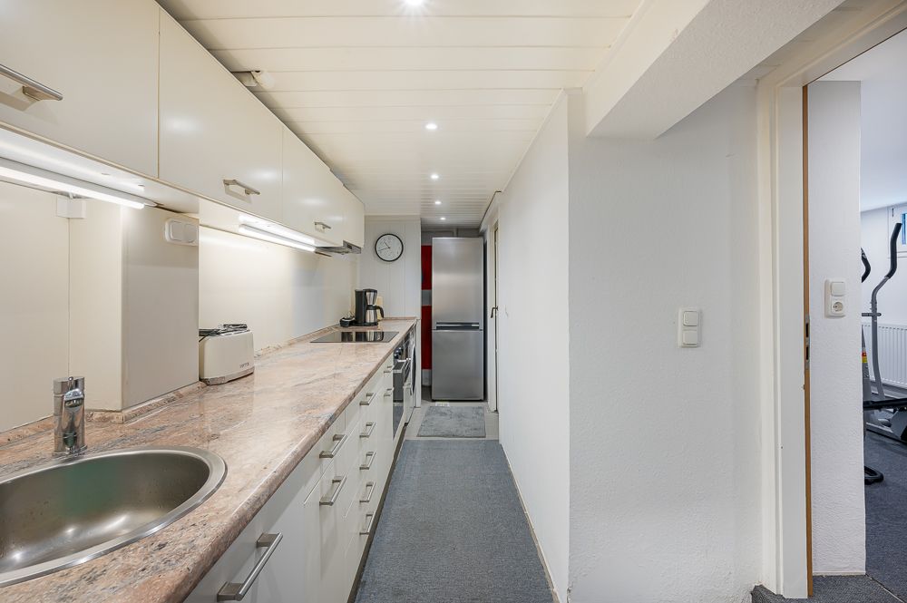 Schlanke Küche mit weißer Einrichtung, Spüle, Geräten und Blick auf einen Kühlschrank am Ende.