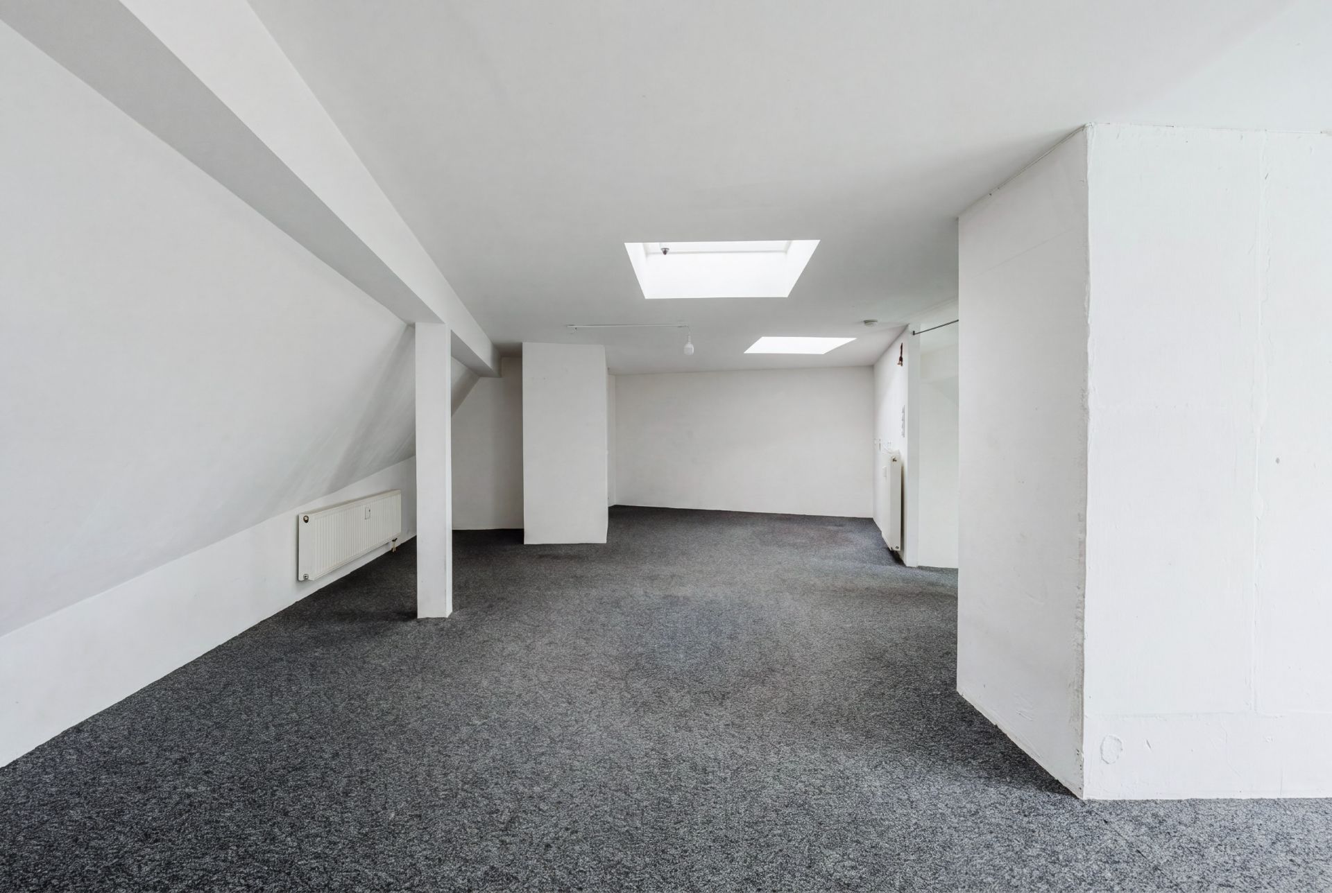 Heller Dachbodenraum mit Teppichboden, weißen Wänden und zwei Dachfenstern.