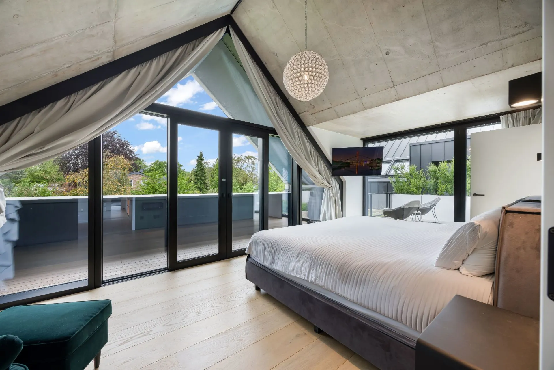 Modernes Schlafzimmer mit großem Bett, Glasfront und Zugang zu einem Balkon mit Ausblick ins Grüne.