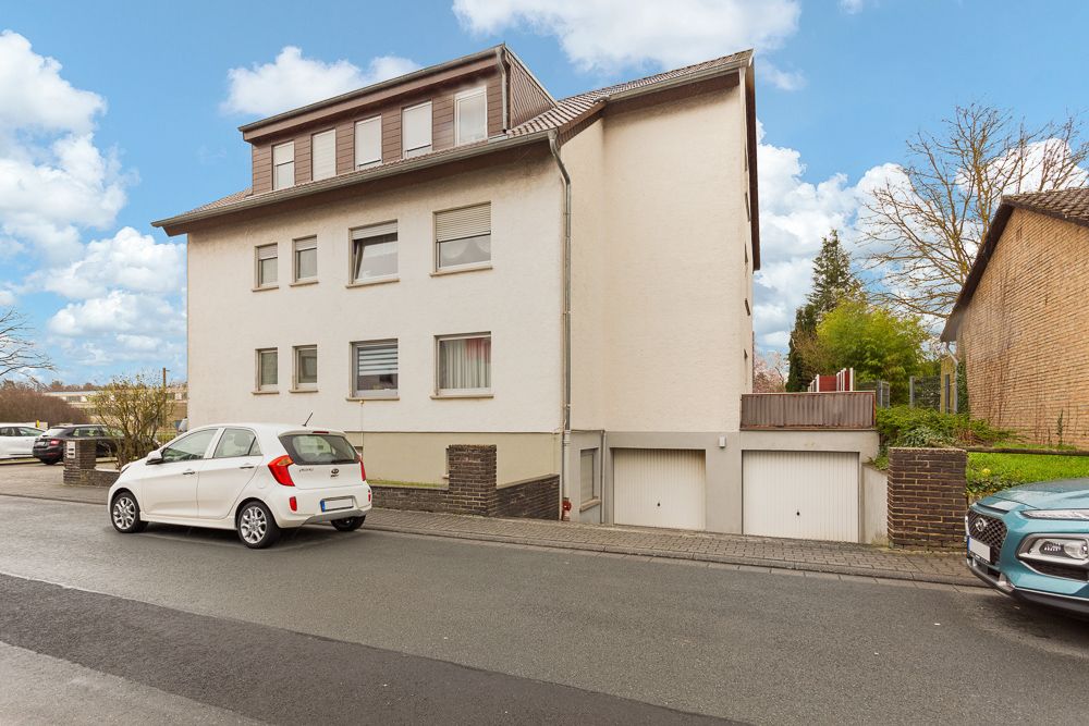 Mehrfamilienhaus mit weißen Wänden, Satteldach und zwei Garagentoren an der Straßenseite.