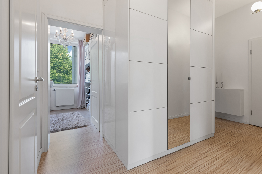 Heller Flur mit Einbauschrank, Blick in ein Zimmer mit Regal, Teppich und großem Fenster.