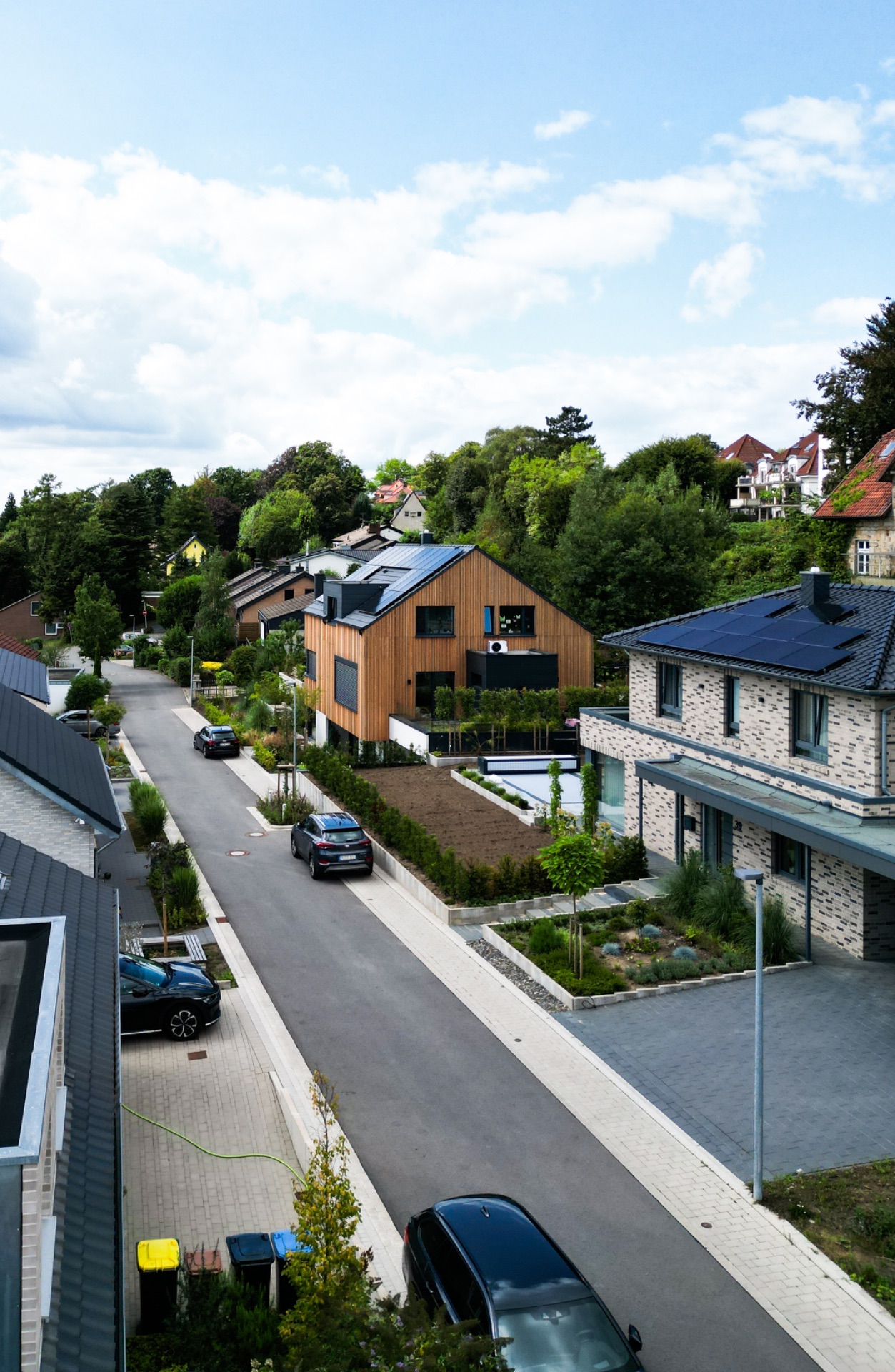Moderne Wohnstraße mit Autos, Einfamilienhäusern und viel Grün an einem sonnigen Tag.