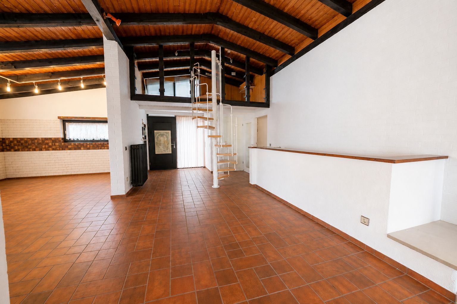 Wohnraum mit offener Küche, Wendeltreppe und Galerie, Holzbalkendecke, Fliesenboden.