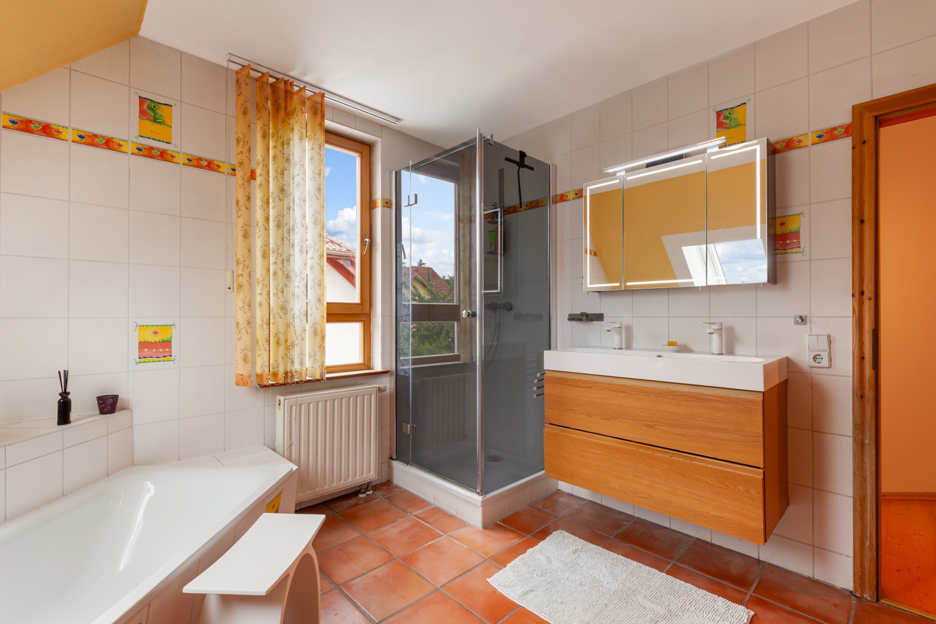 Modernes Badezimmer mit Badewanne, Dusche, Doppelwaschbecken, Fenster und Fliesenboden.