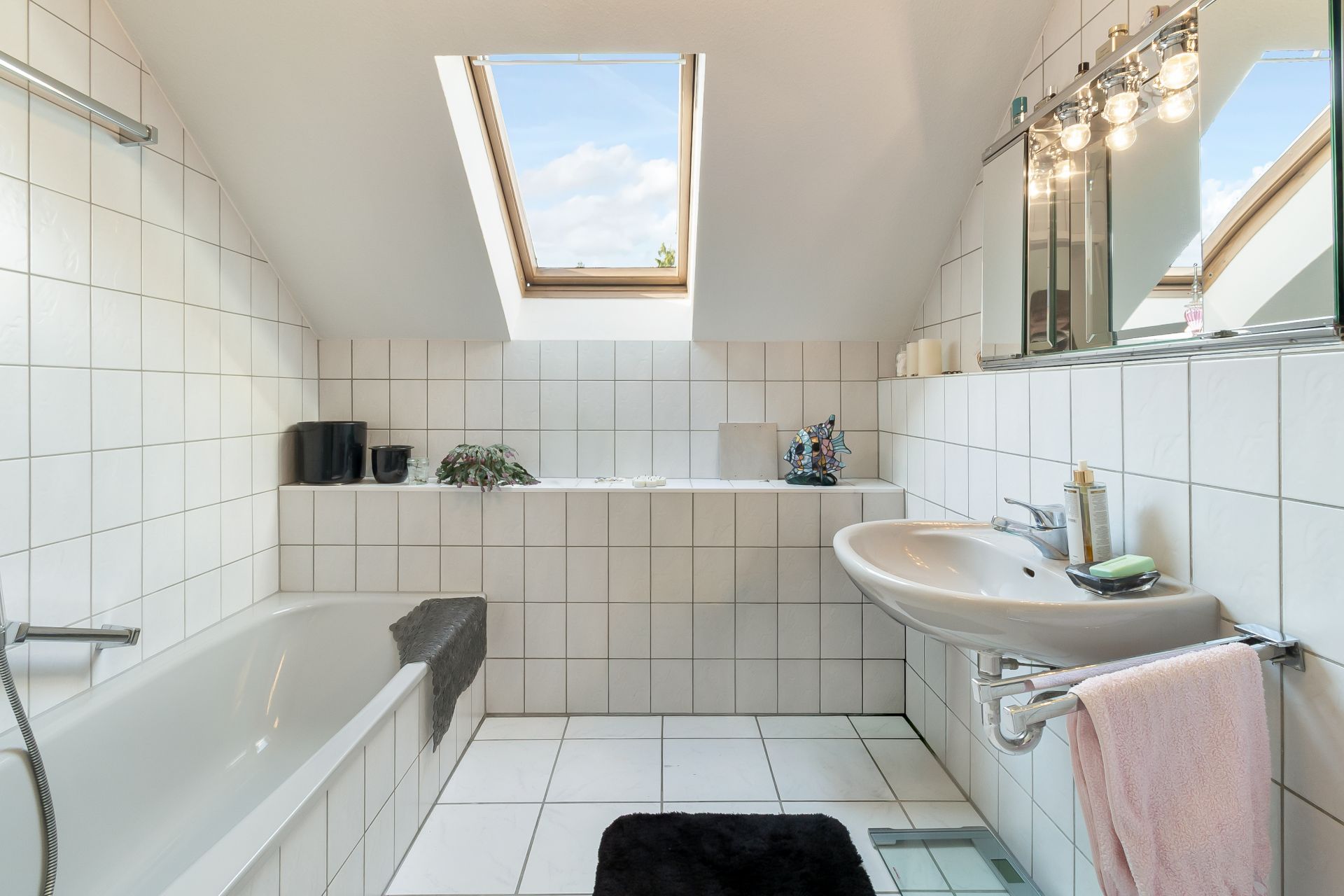Helles Badezimmer mit Badewanne, Waschbecken, Spiegel und Dachfenster.