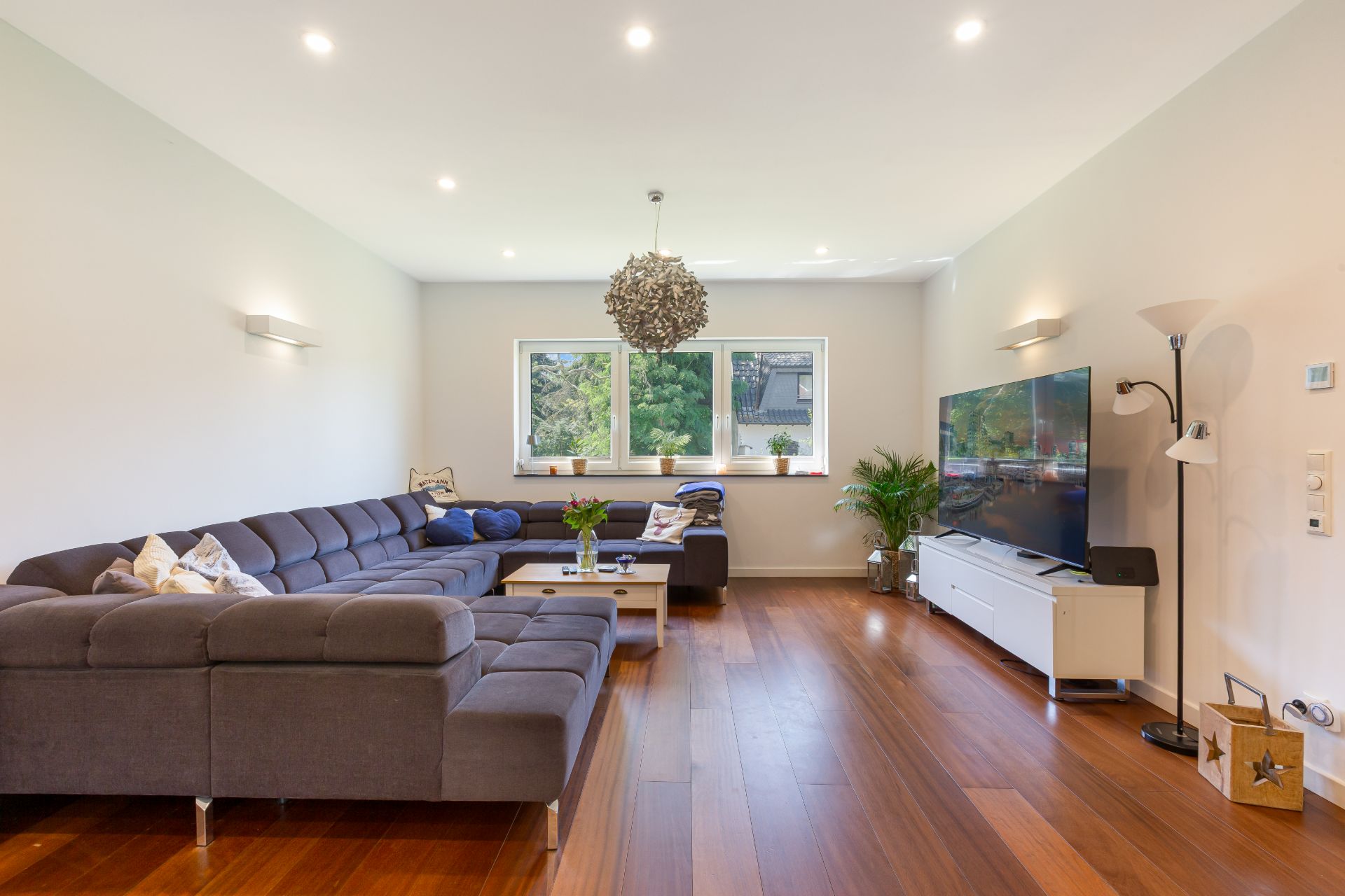 Modernes Wohnzimmer mit großem Ecksofa, Couchtisch, Fernseher und Holzboden.