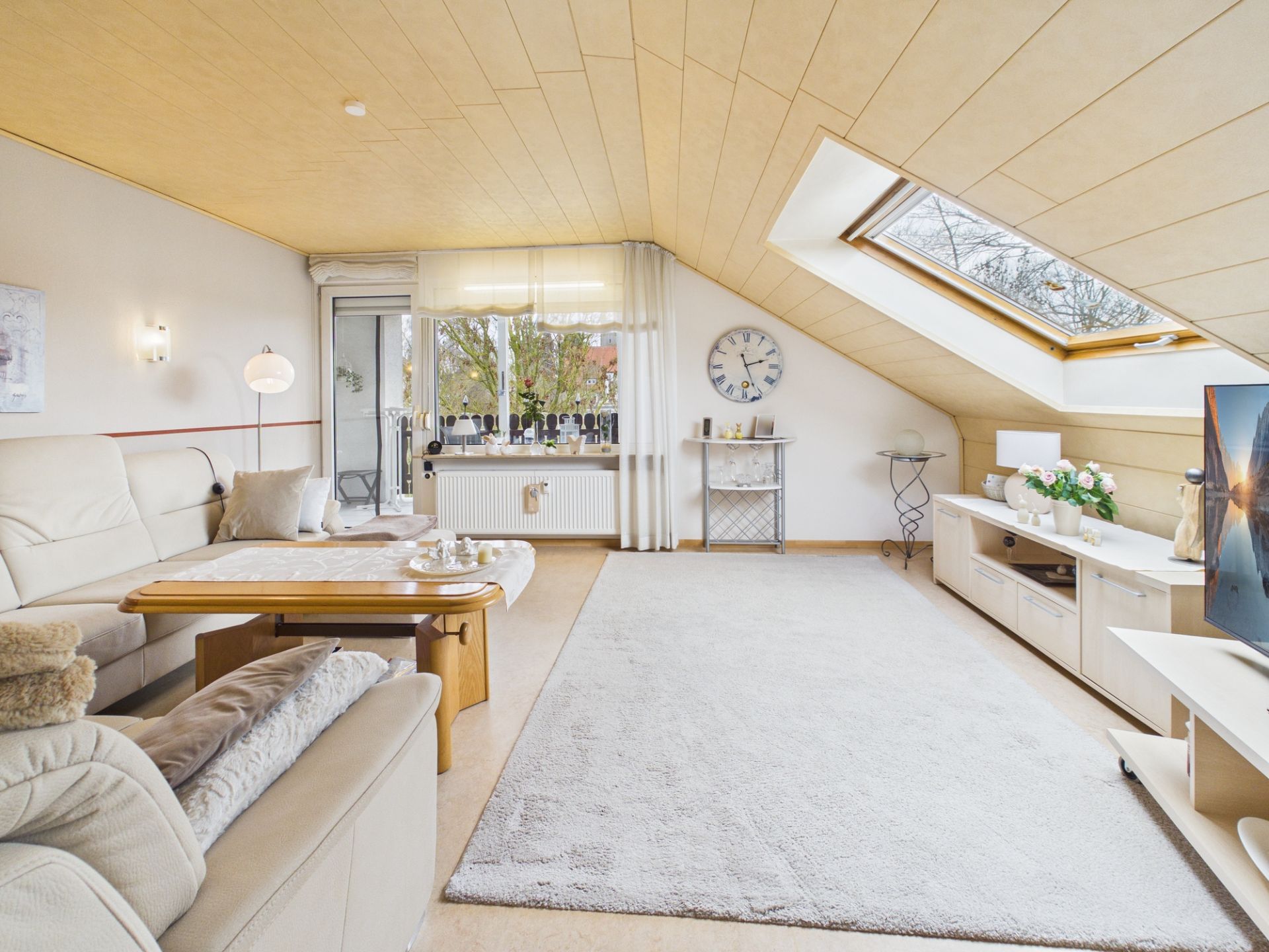Helles Wohnzimmer mit Dachschräge, großen Fenstern, Sofa, Couchtisch und Teppich.