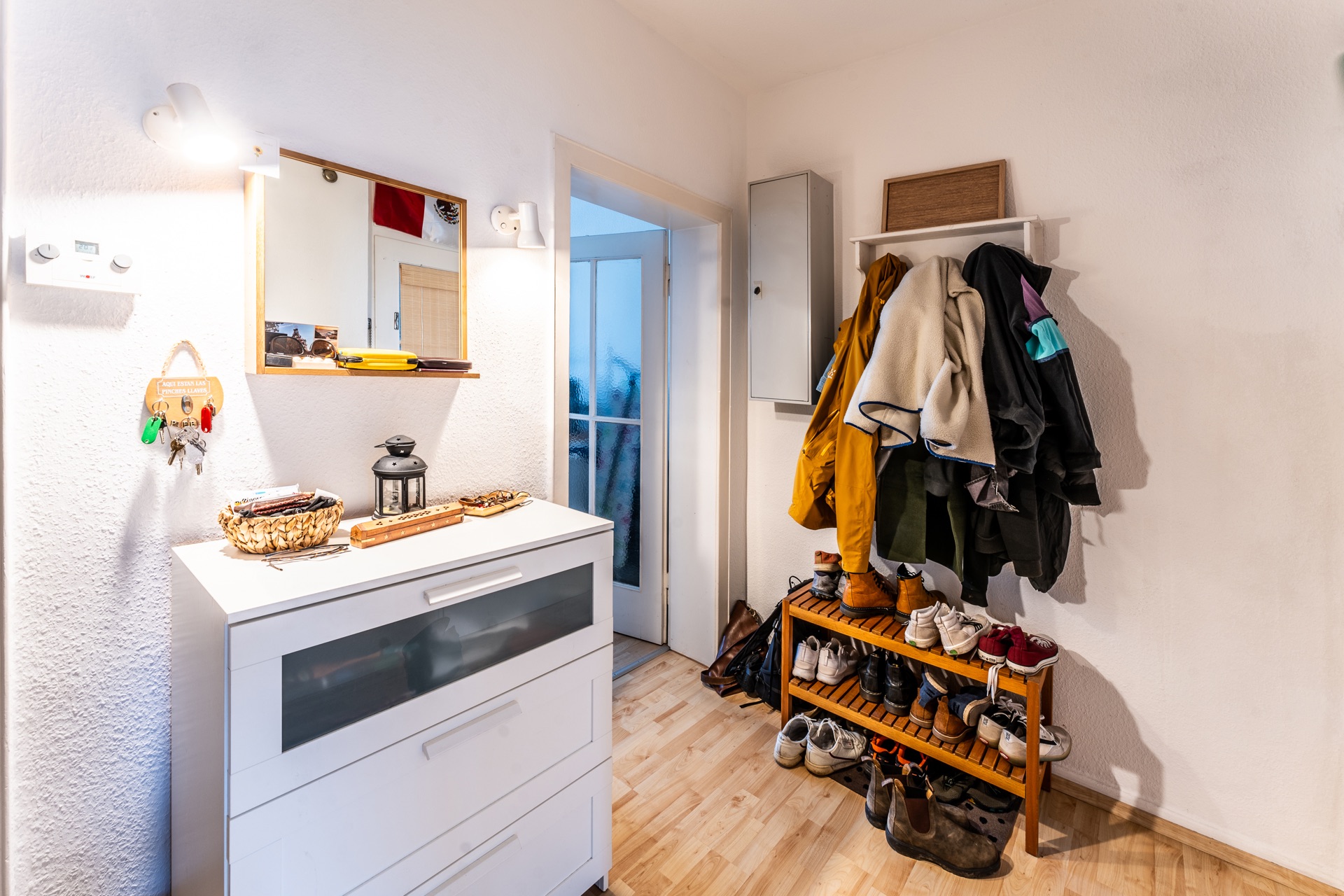 Flur mit Kommode, Spiegel, Schlüsselbrett, Garderobe mit Jacken und Schuhregal mit vielen Schuhen.
