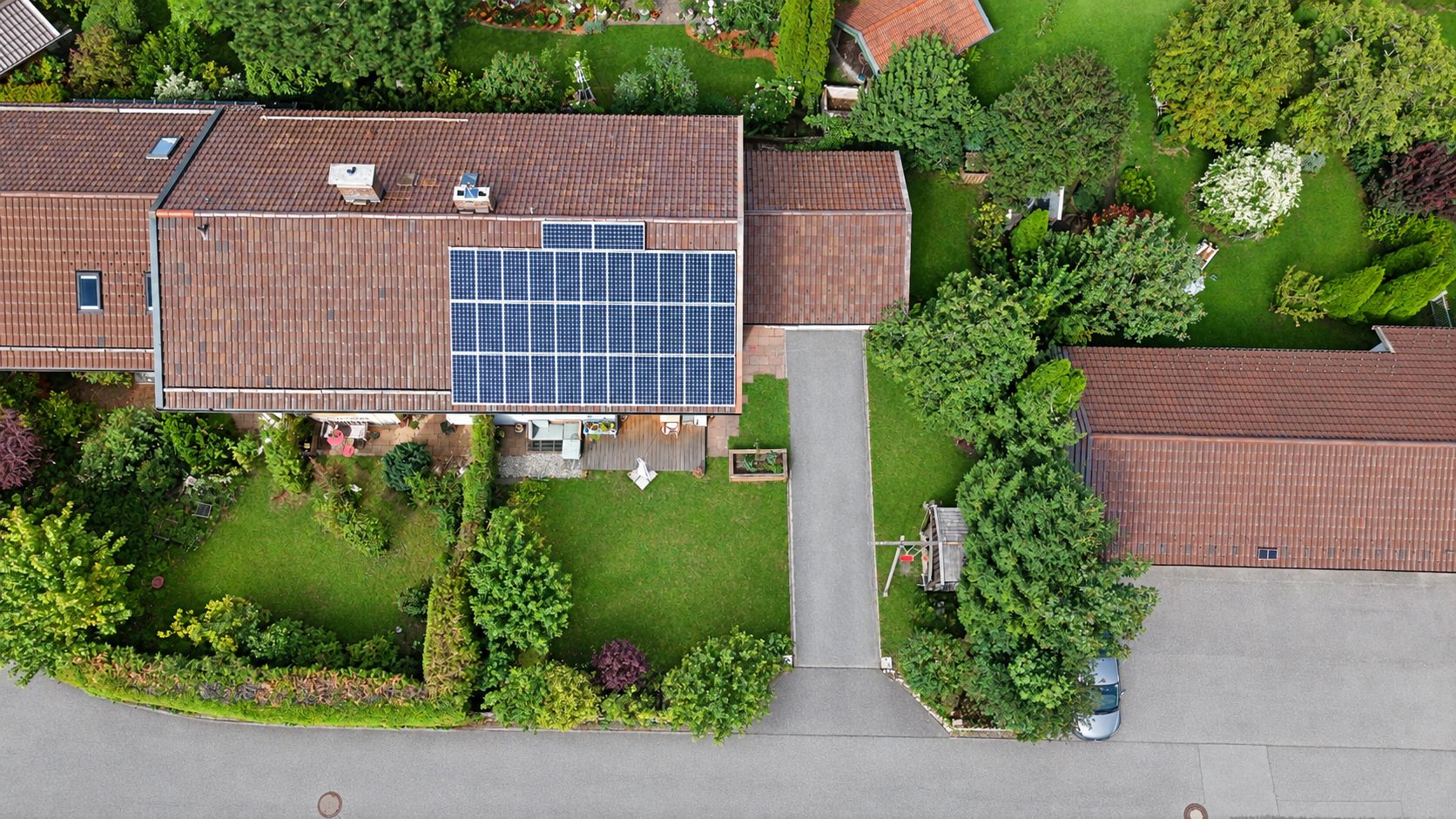 Luftaufnahme eines Wohnhauses mit Solarpanelen auf dem Dach und gepflegtem Garten.