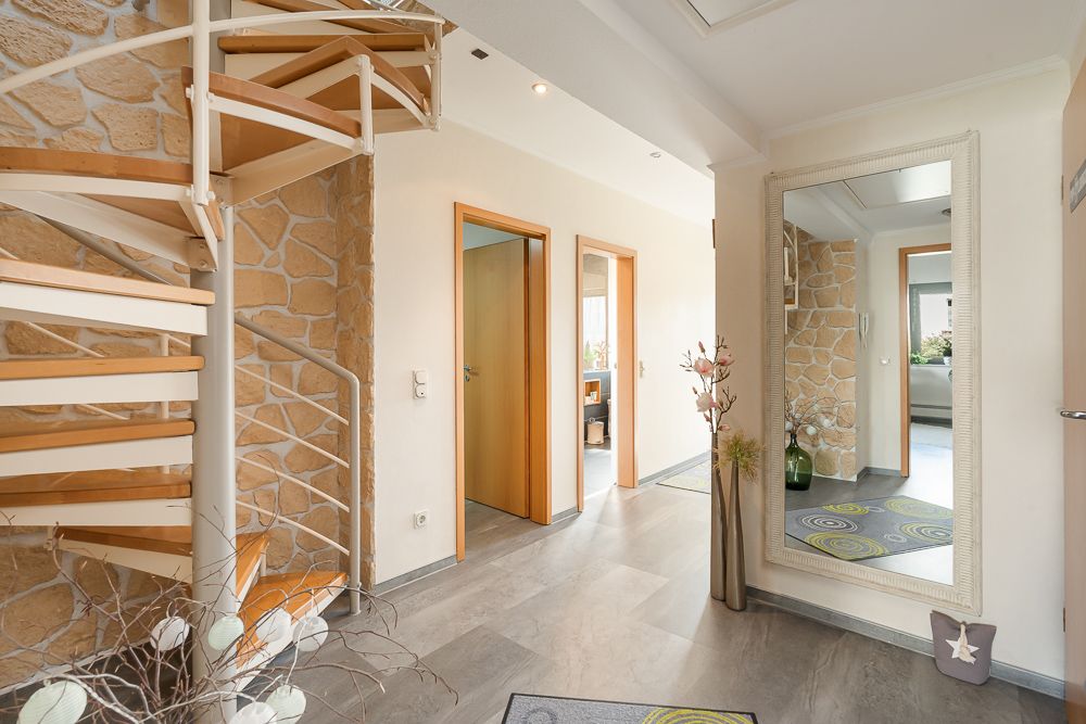 Heller Flur mit Wendeltreppe, großem Spiegel und zwei offenen Türen.