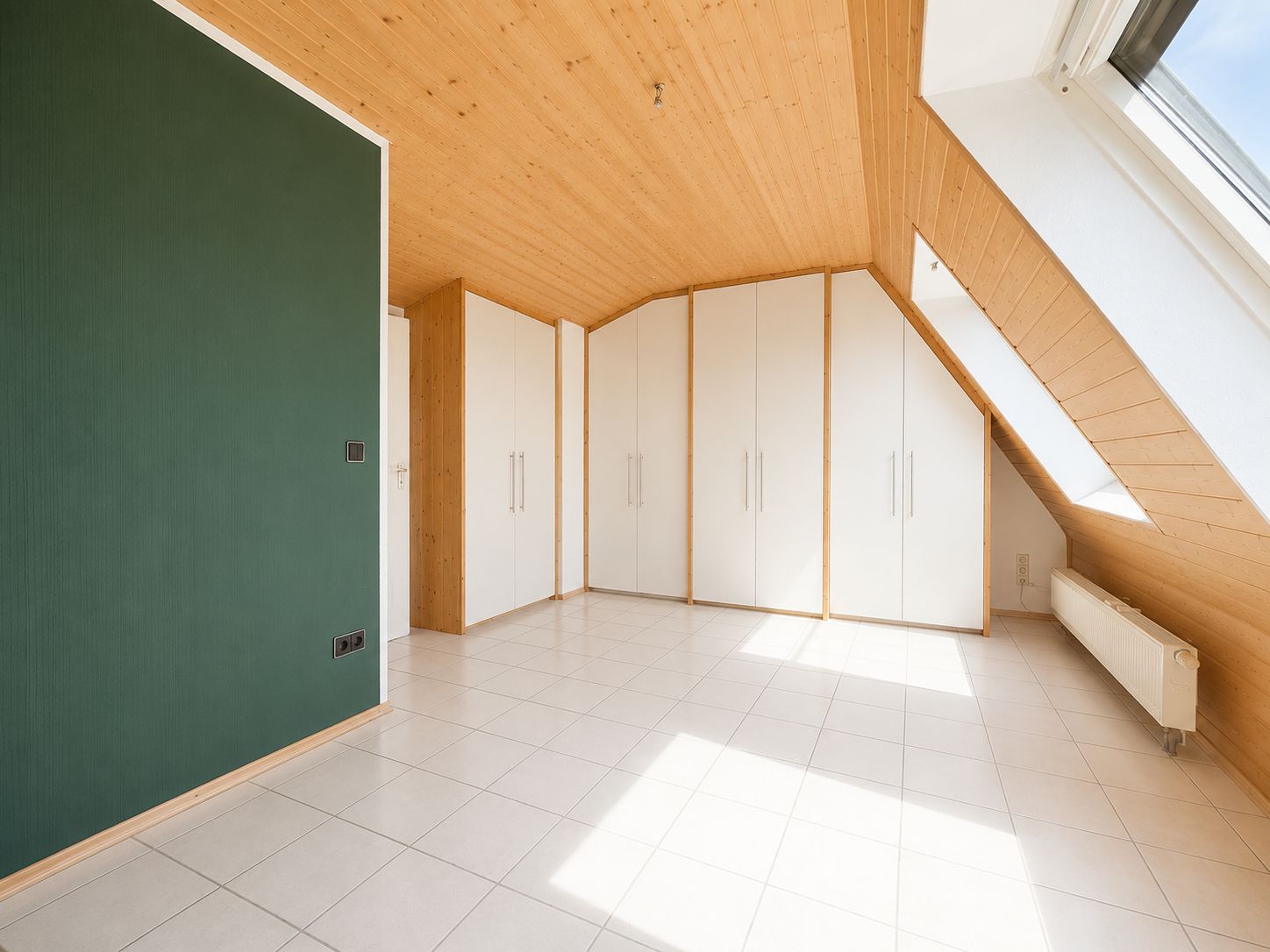 Heller Dachraum mit weißen Einbauschränken, Fliesenboden und Dachfenster.