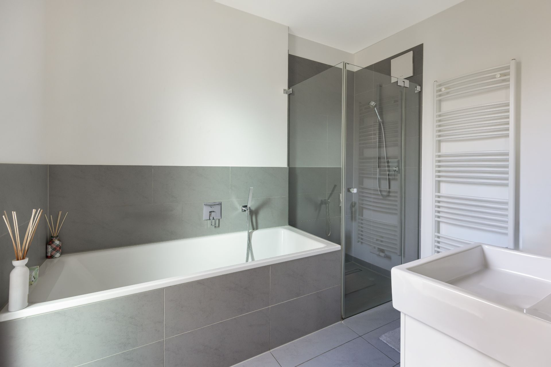 Modernes Badezimmer mit Badewanne, Dusche, Waschbecken und Handtuchheizkörper.