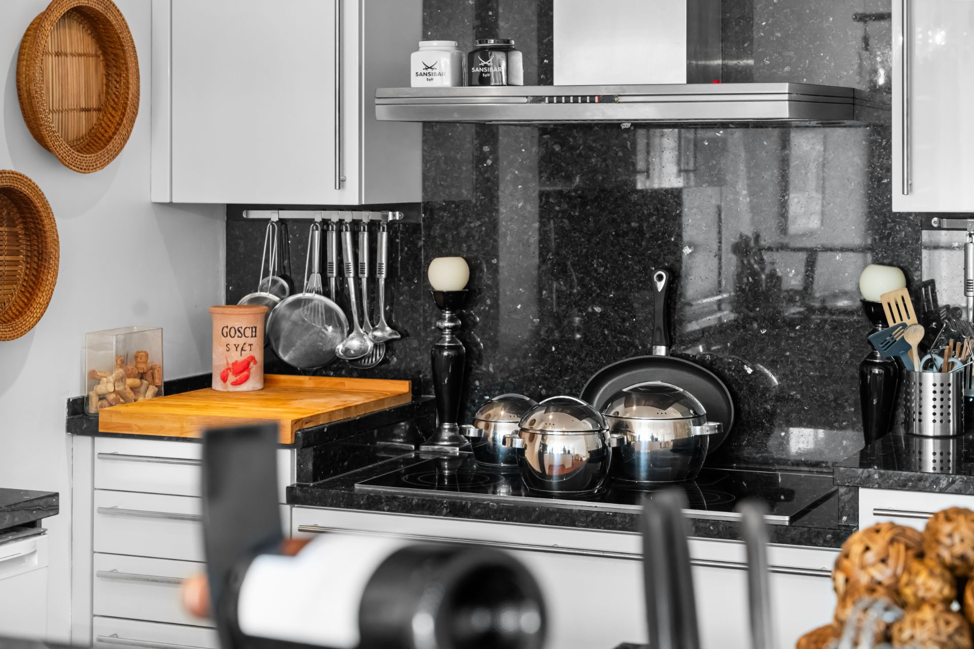 Moderne Küche mit Kochfeld, Töpfen, Besteckhalter und Schneidebrett.